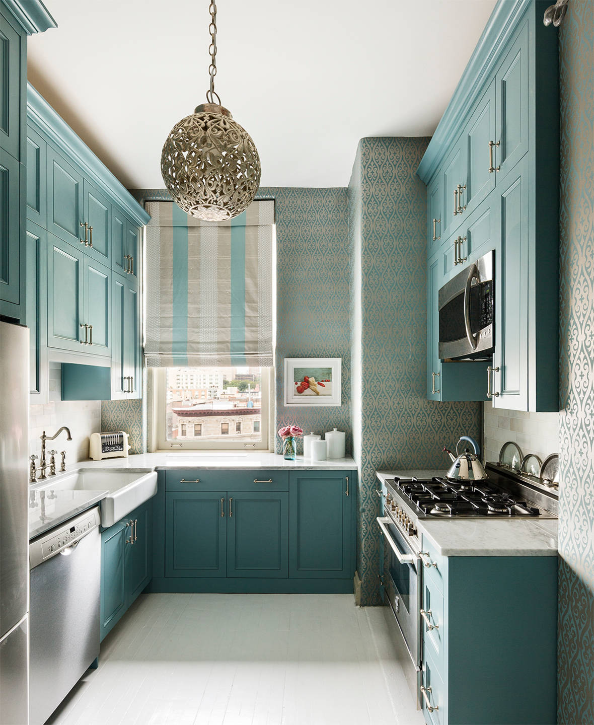 L-shaped kitchen with aqua cabinets, damask wallpaper, ornate pendant light, farmhouse sink, and city window views.