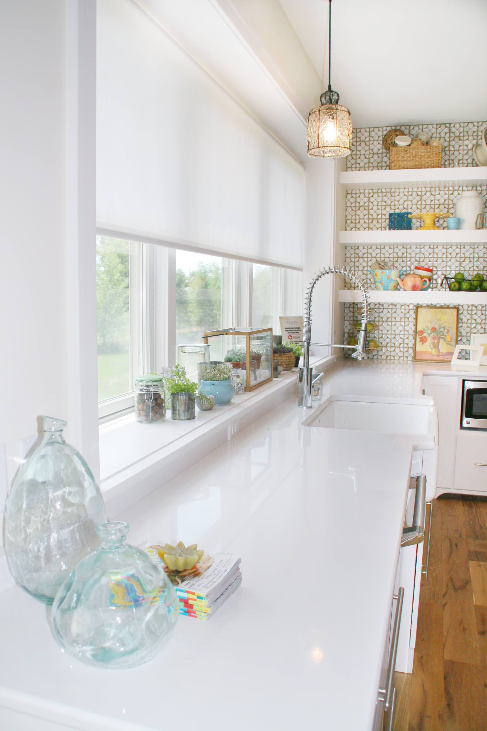 White kitchen with geometric wallpaper, floating shelves, large window, glass jars, and professional faucet against white countertops.