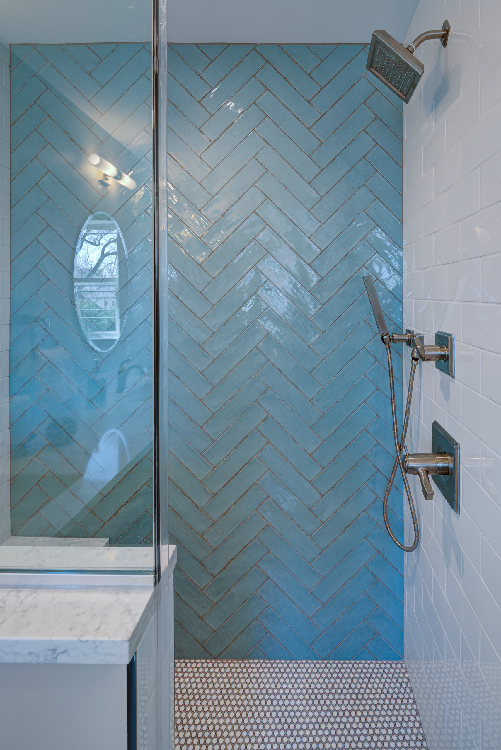 Modern shower featuring aqua herringbone tile wall, glass partition, marble bench, and chrome fixtures with penny tile flooring.