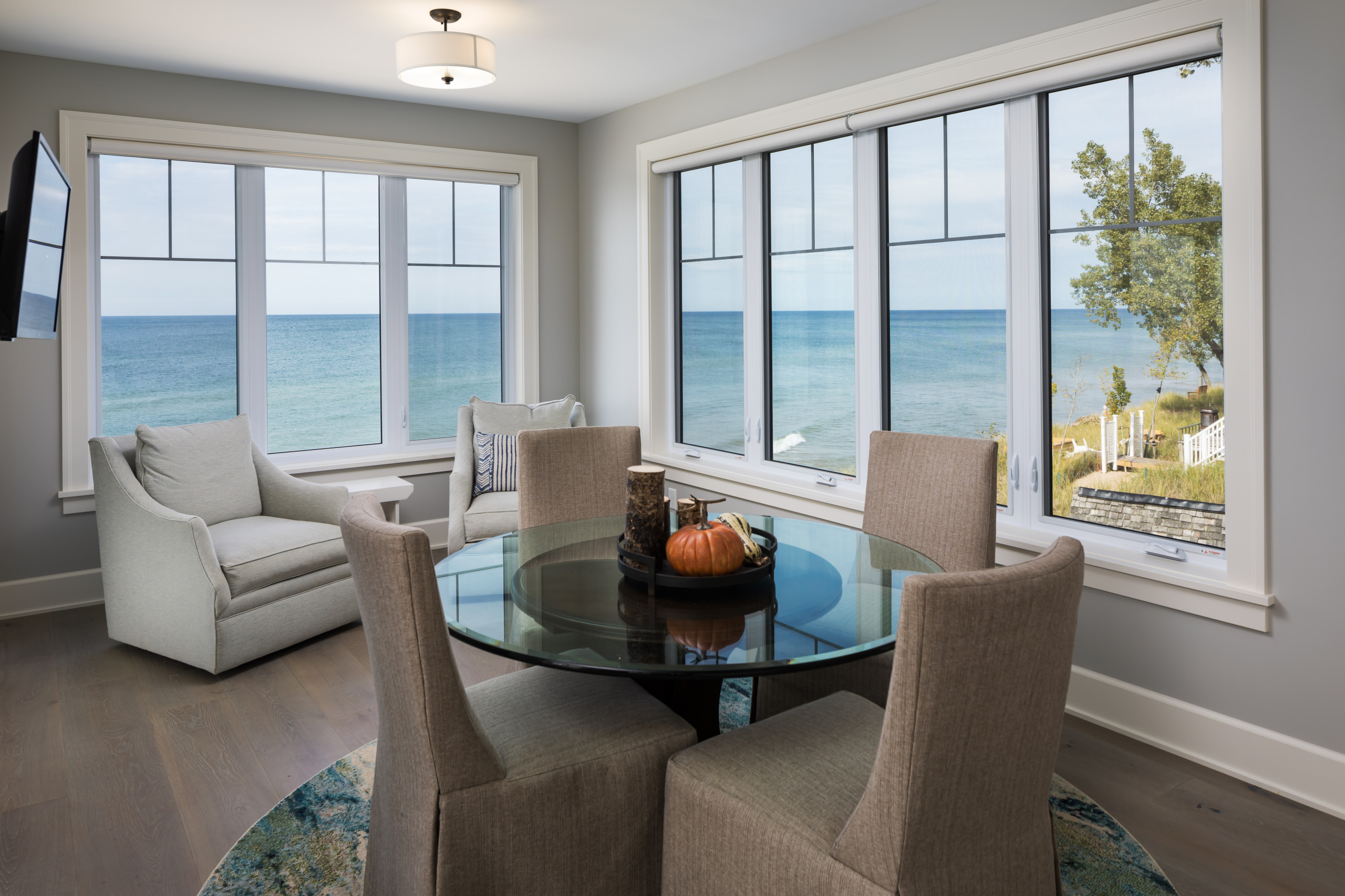 Breakfast nook with glass dining table, upholstered chairs, and panoramic windows overlooking lake waters and coastal landscape.