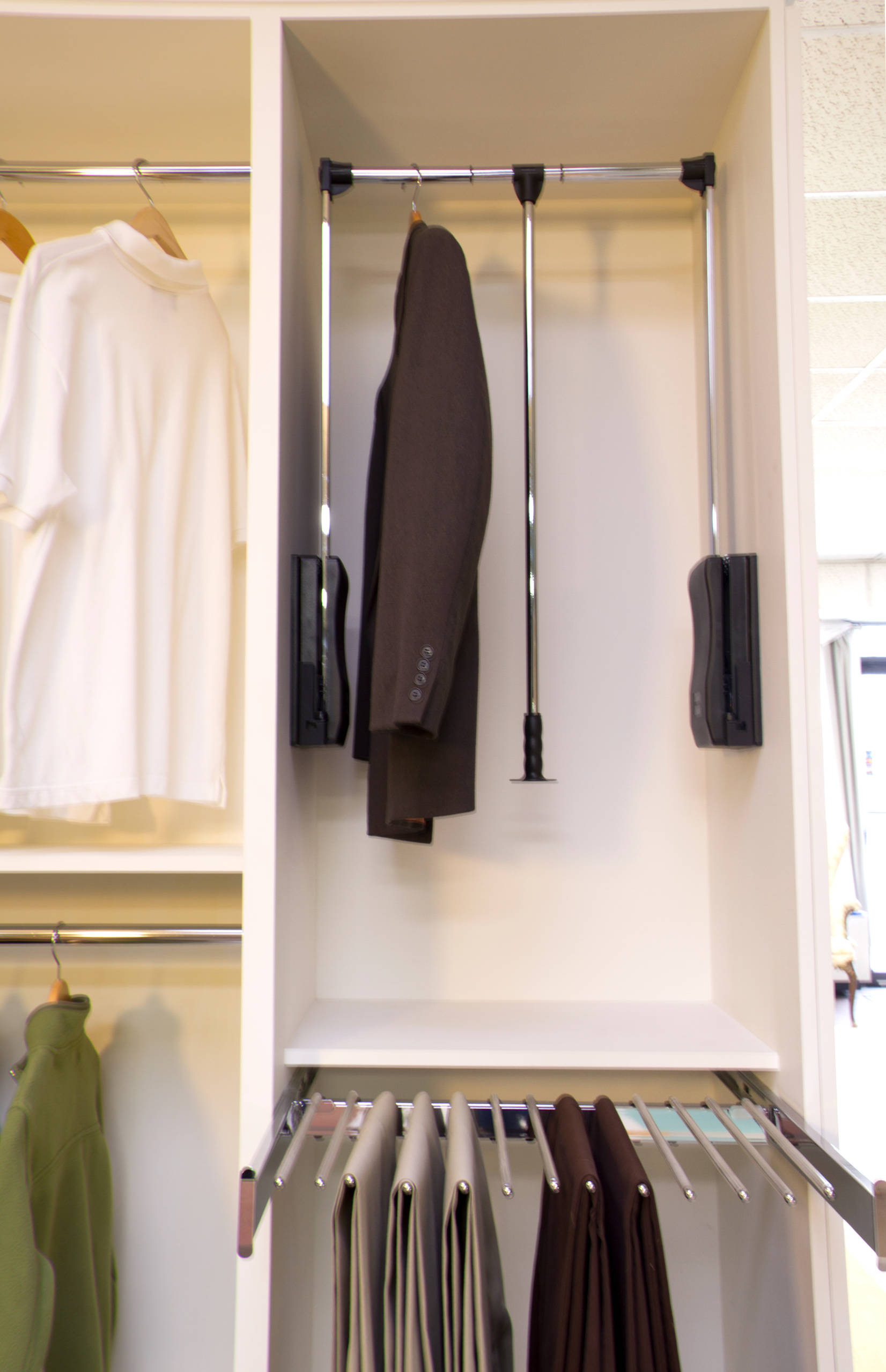 White closet system featuring pull-down clothing rod, trouser rack, and organized compartments for suits and casual wear.