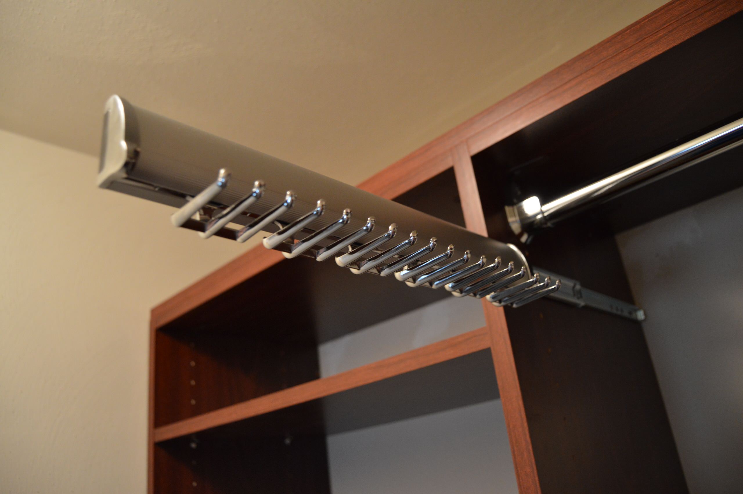 Chrome pull-out tie rack mounted inside cherry wood closet cabinet with adjustable shelving and cream walls.