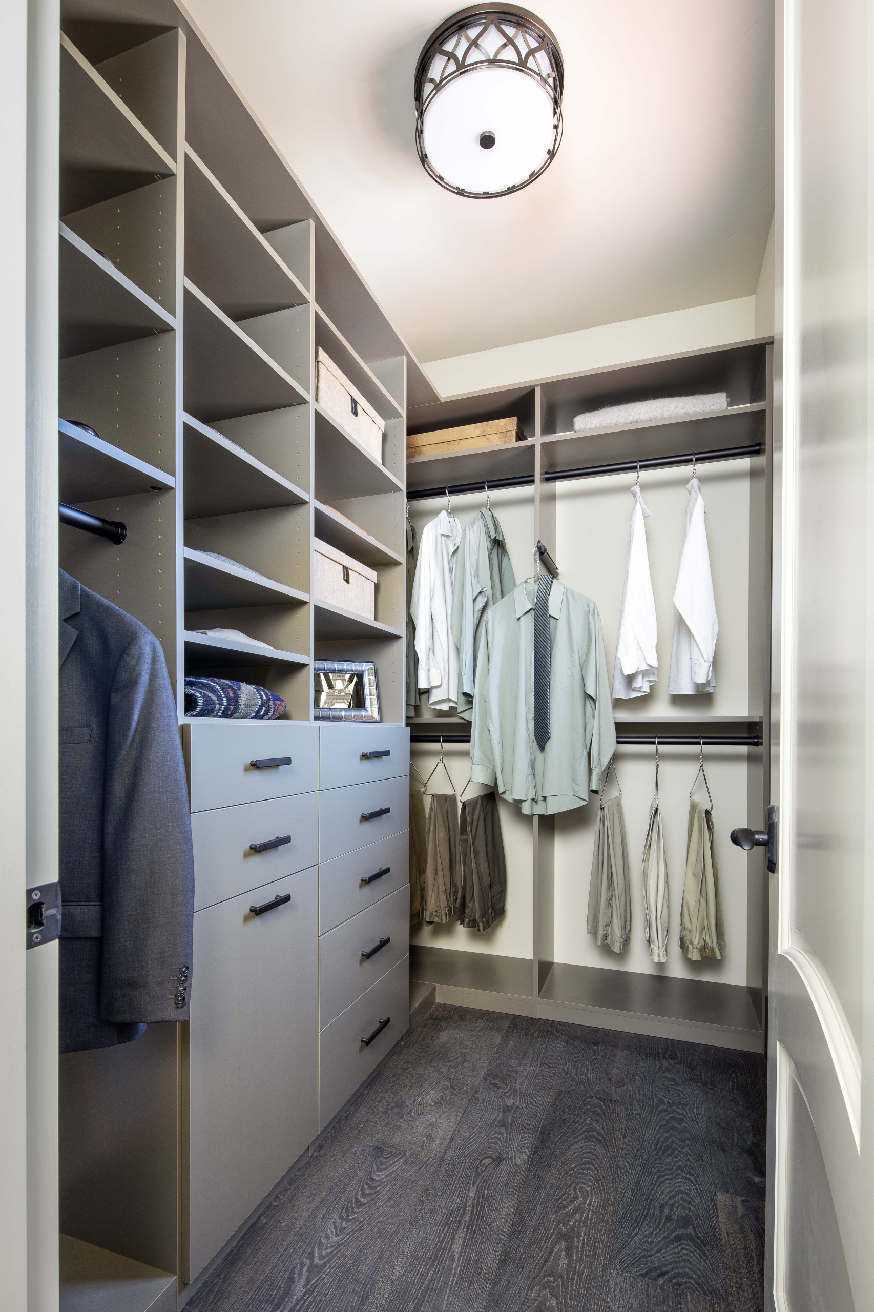 Walk-in closet with taupe built-in shelving, light blue drawers, hanging rods, and decorative ceiling fixture on dark wood flooring.