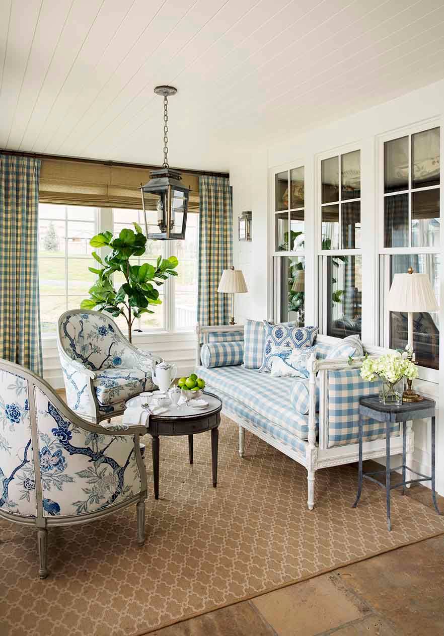 Sunroom featuring blue and white toile chairs, gingham daybed, lantern pendant, and fiddle leaf fig plant against white walls.