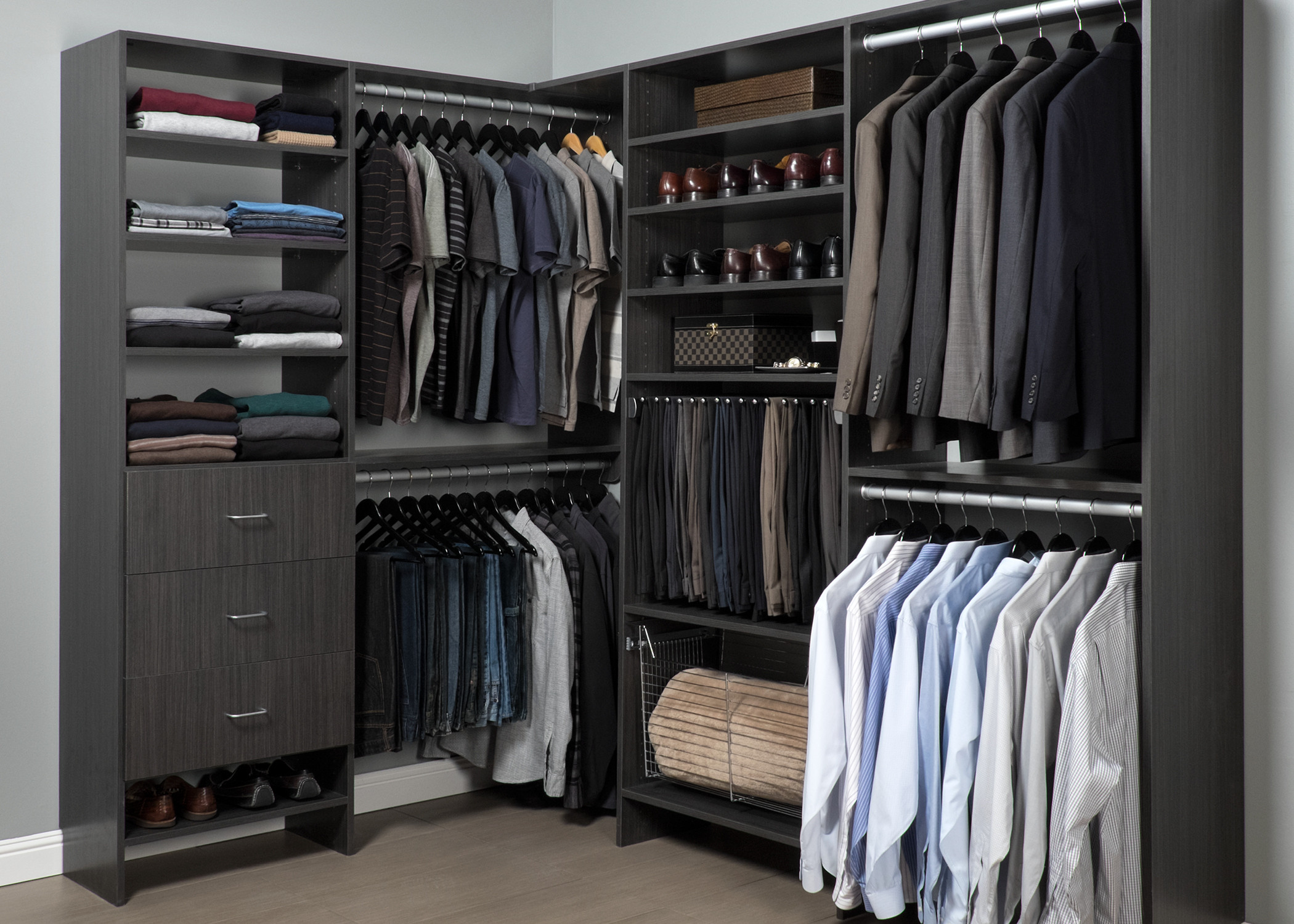 L-shaped walk-in closet with charcoal wood cabinetry featuring organized suits, shirts, shoes, and accessories in muted color palette.