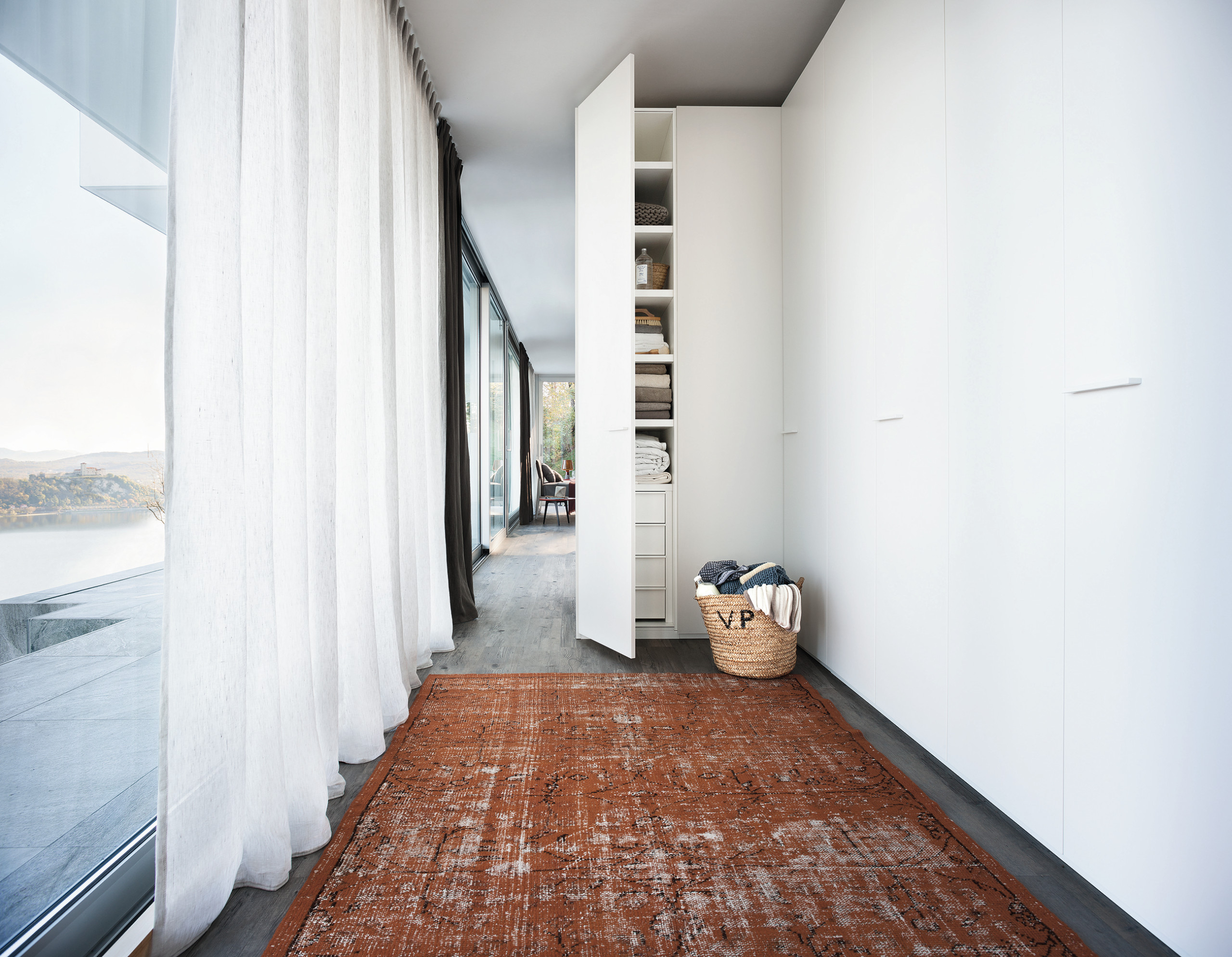 Minimalist corridor with floor-to-ceiling windows, white built-in storage, terracotta rug, and panoramic lake views.
