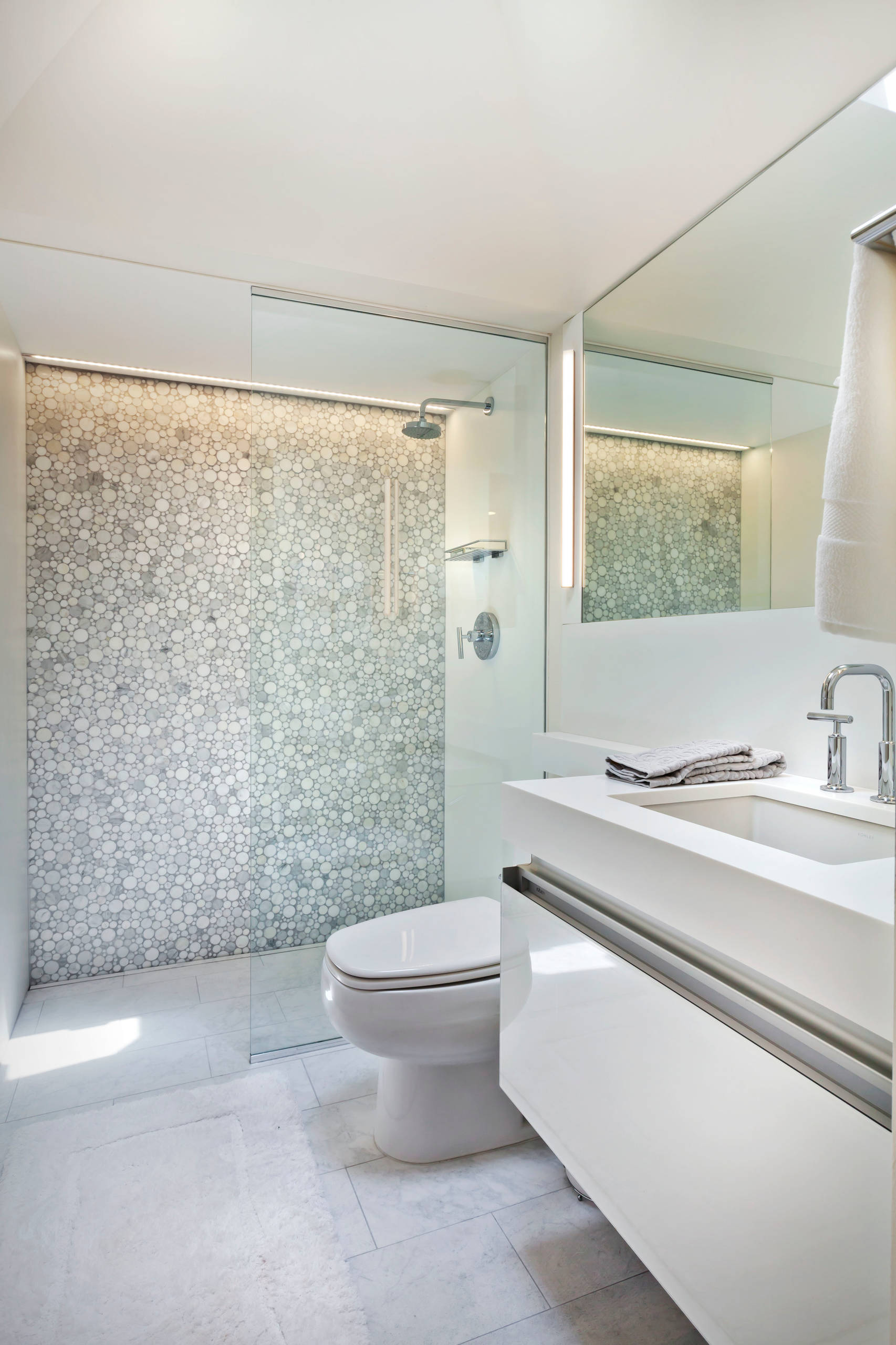 Modern white bathroom featuring circular mosaic shower wall, floating vanity, and glass partition with chrome fixtures.