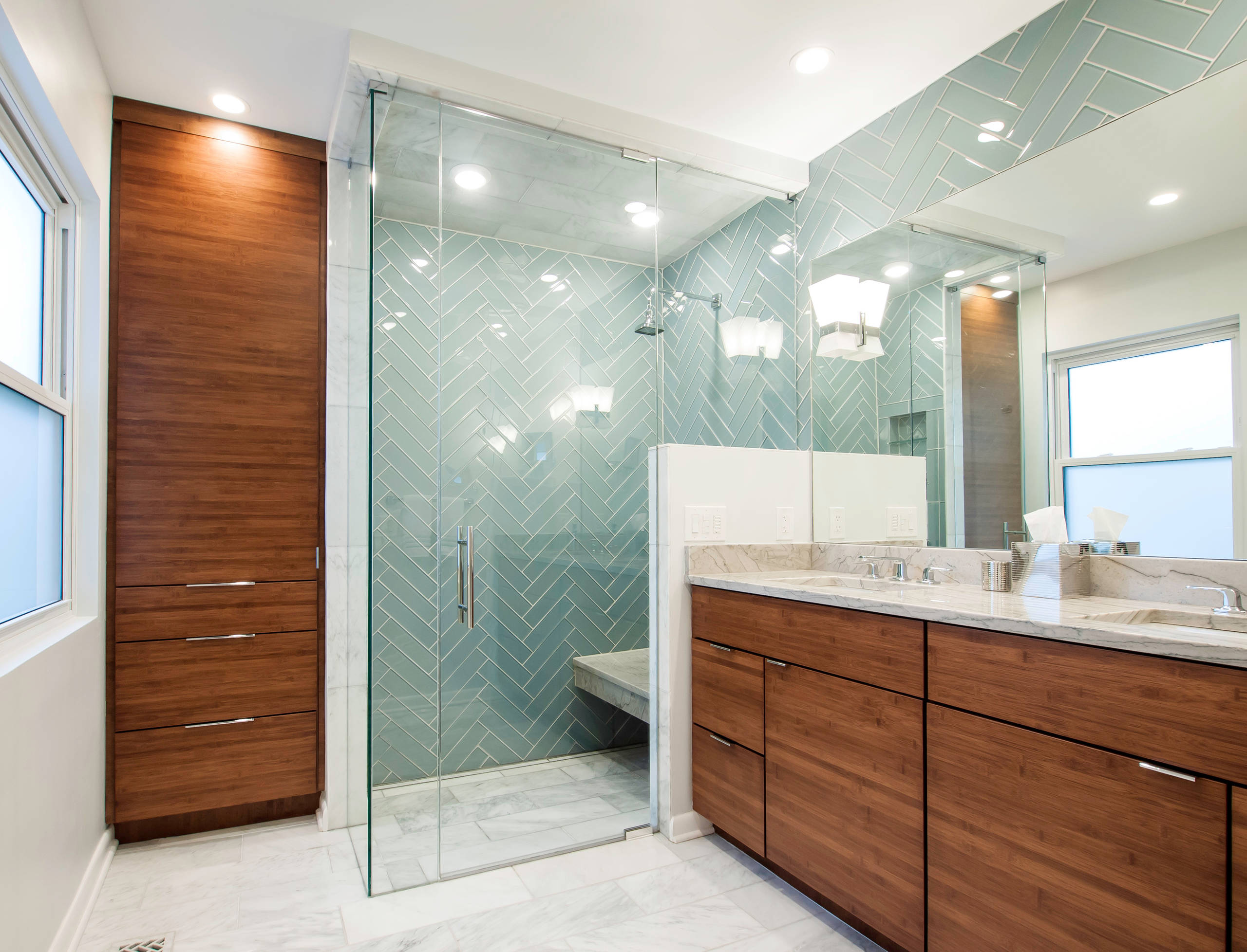 Modern bathroom featuring mint herringbone shower tiles, walnut cabinetry, marble countertops, and frameless glass shower enclosure.