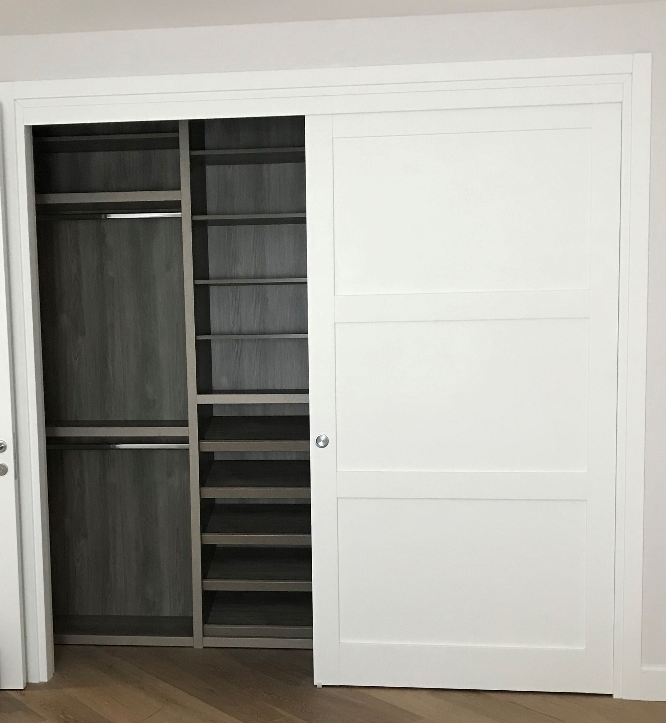 Built-in closet featuring charcoal gray interior shelving, hanging rods, and crisp white sliding door with paneled detail.