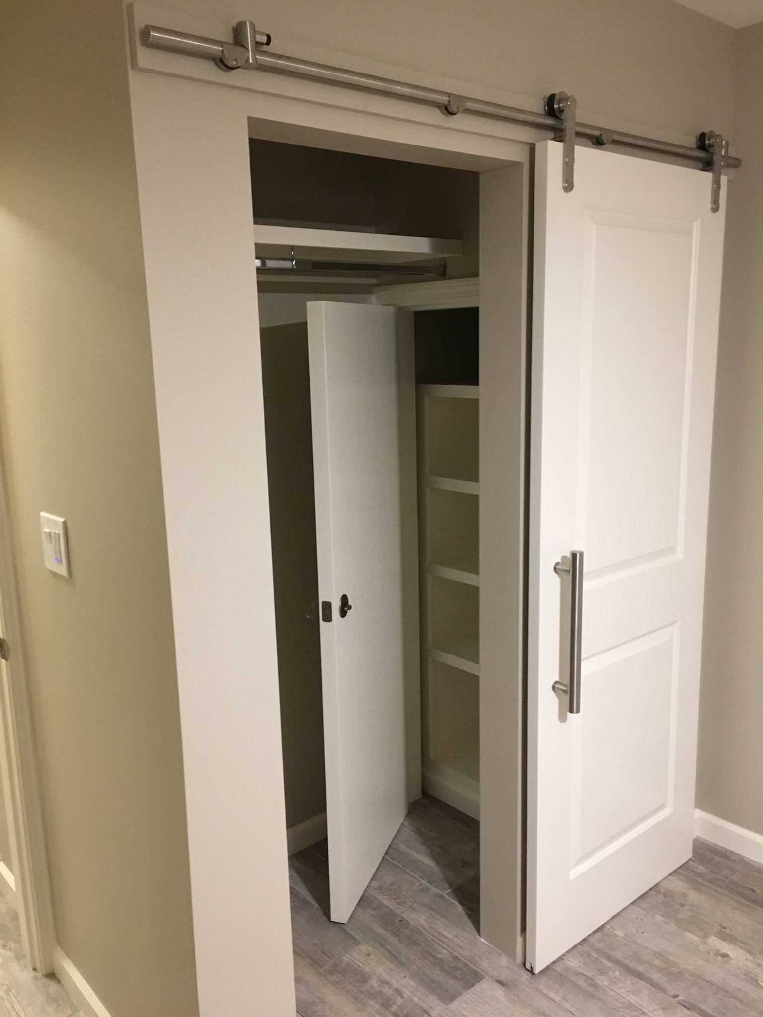 White sliding barn door with stainless steel hardware revealing organized closet space with built-in shelving and gray wood-look flooring.