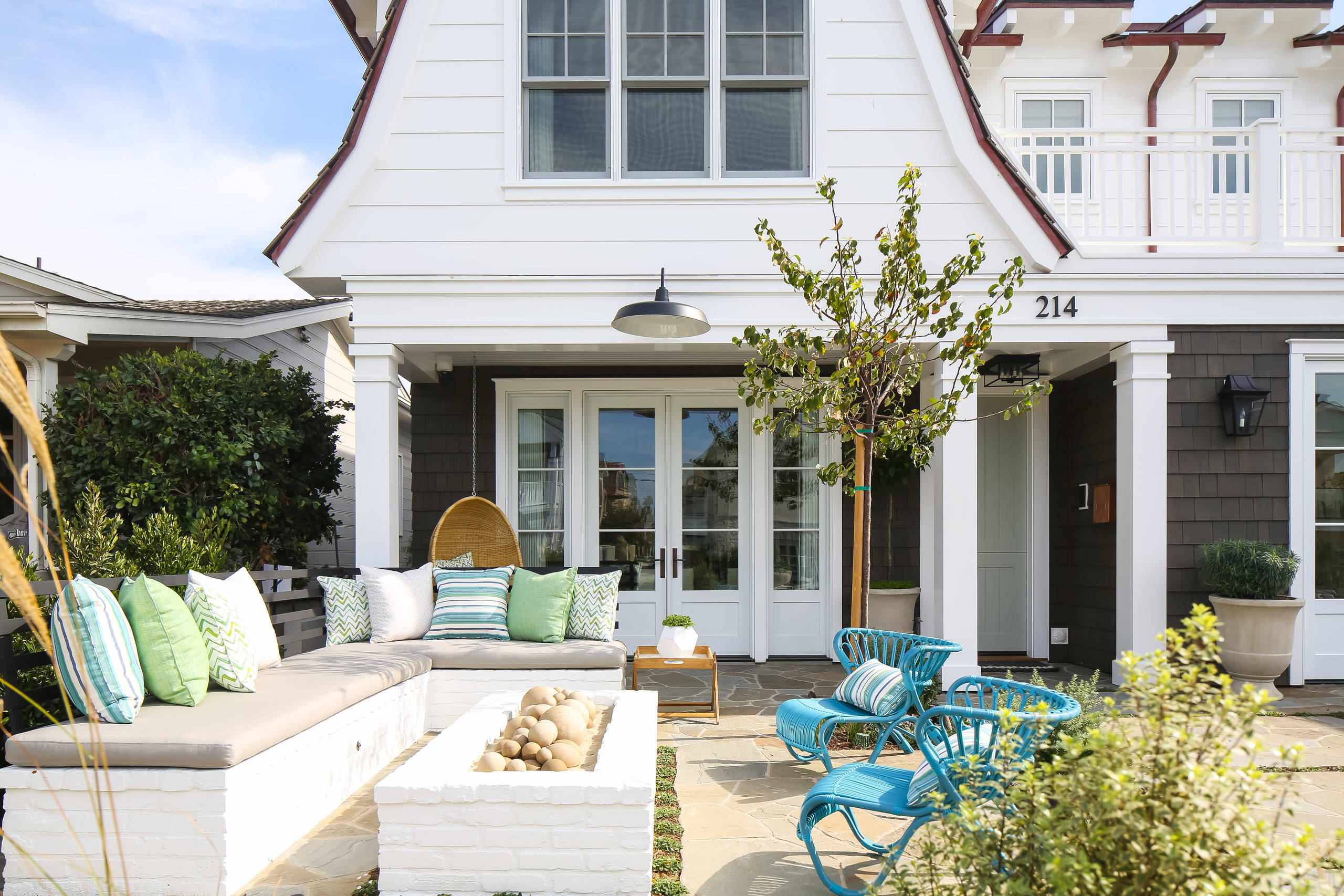 Modern coastal porch featuring built-in white bench seating, turquoise rattan chairs, and stone flooring against white craftsman exterior.
