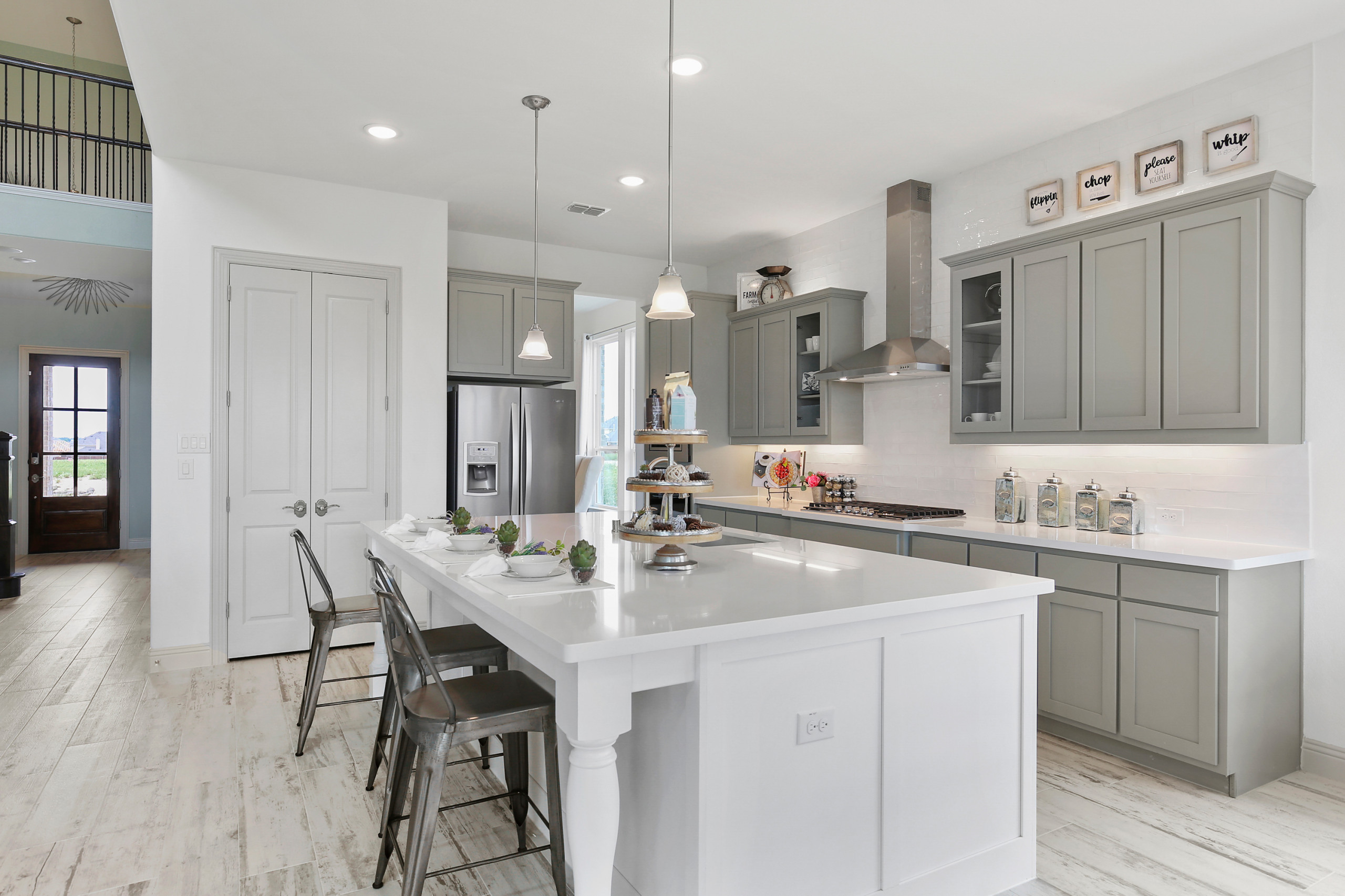 Modern farmhouse kitchen with dove gray cabinets, white quartz island, industrial barstools, and whitewashed wood floors.