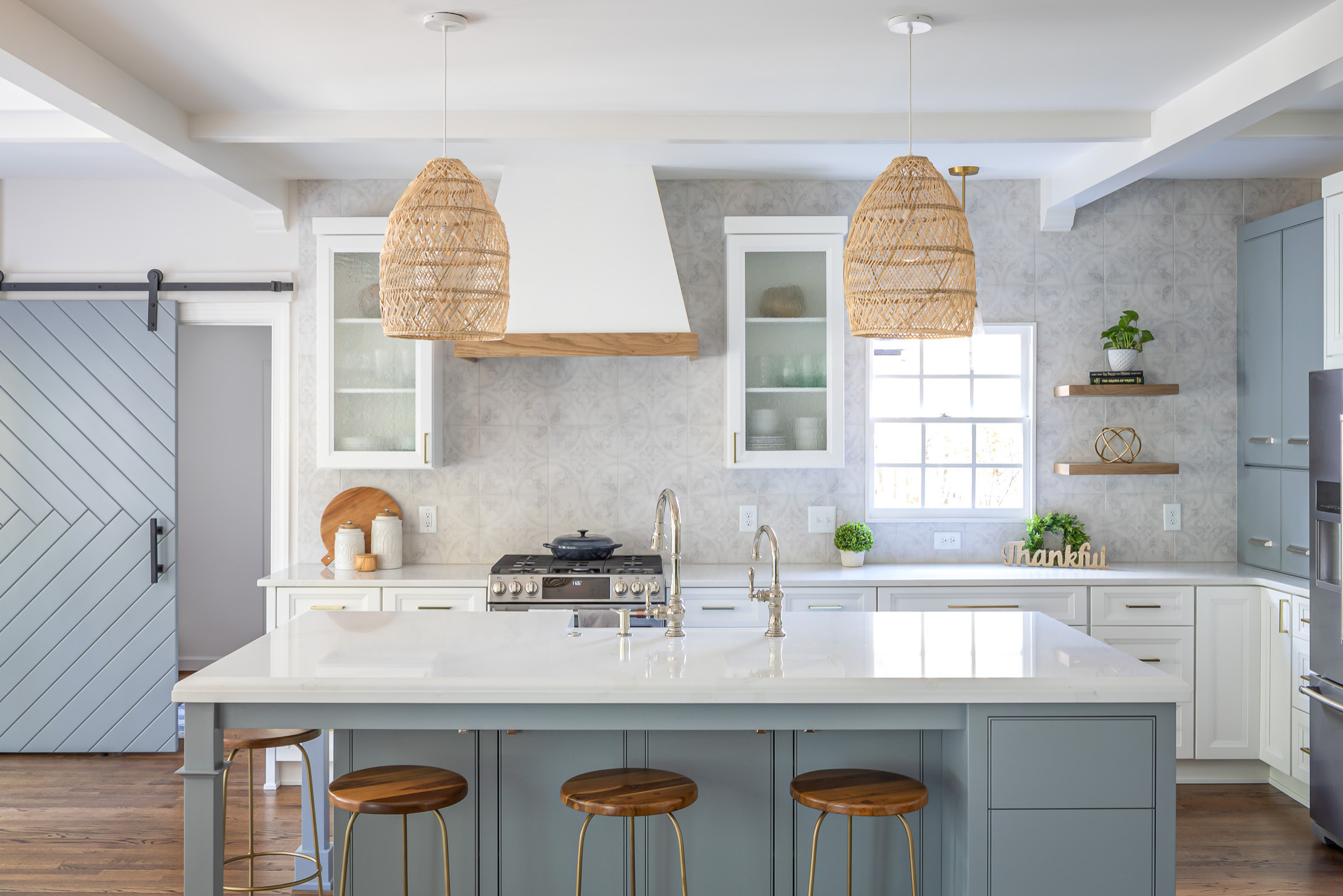 Modern farmhouse kitchen with oversized woven pendant lights, blue-gray island, white quartz countertops, and sliding barn door.