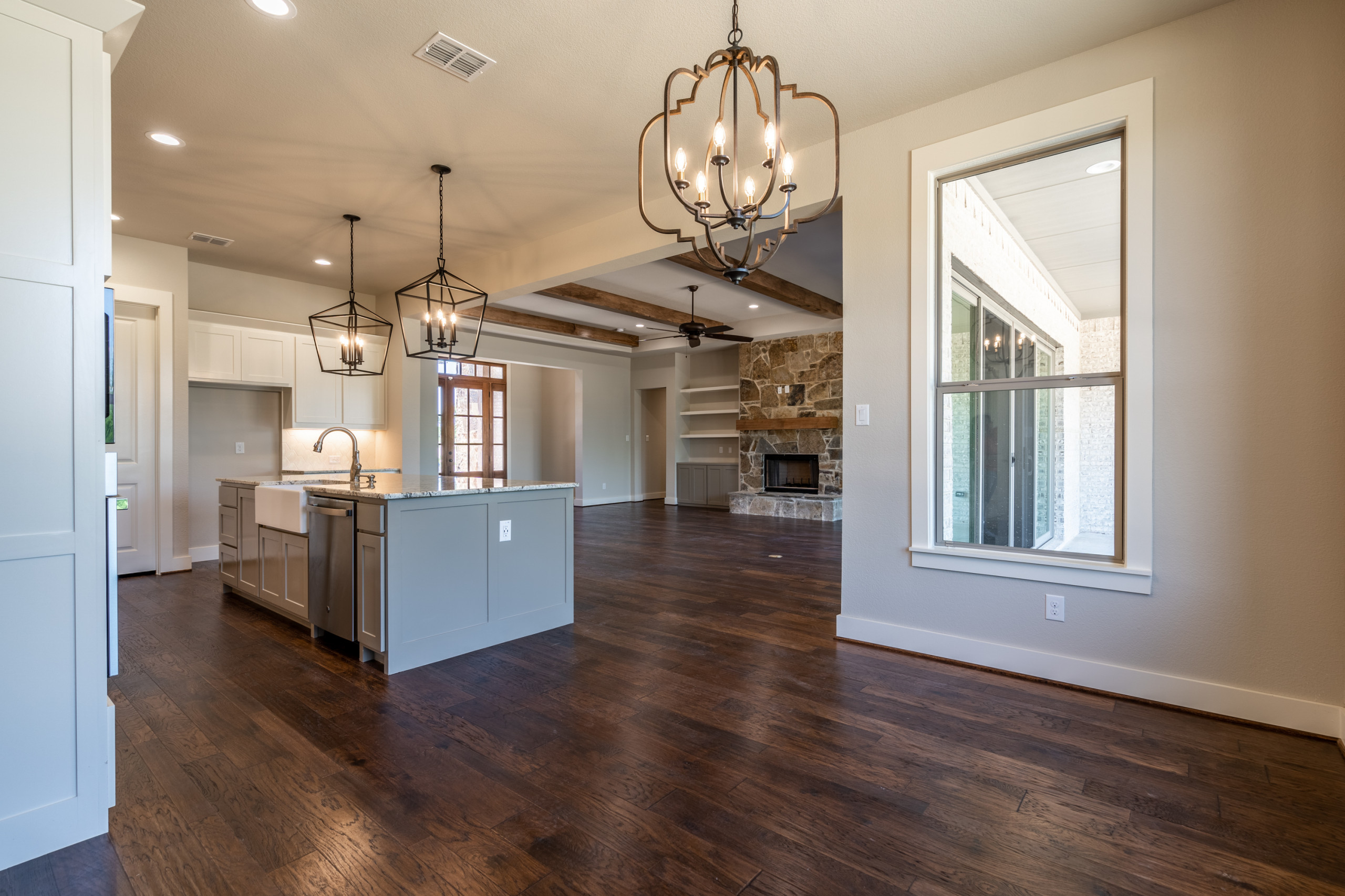 Open-concept living space with gray kitchen island, stone fireplace, dark hardwood floors, and geometric pendant lighting.