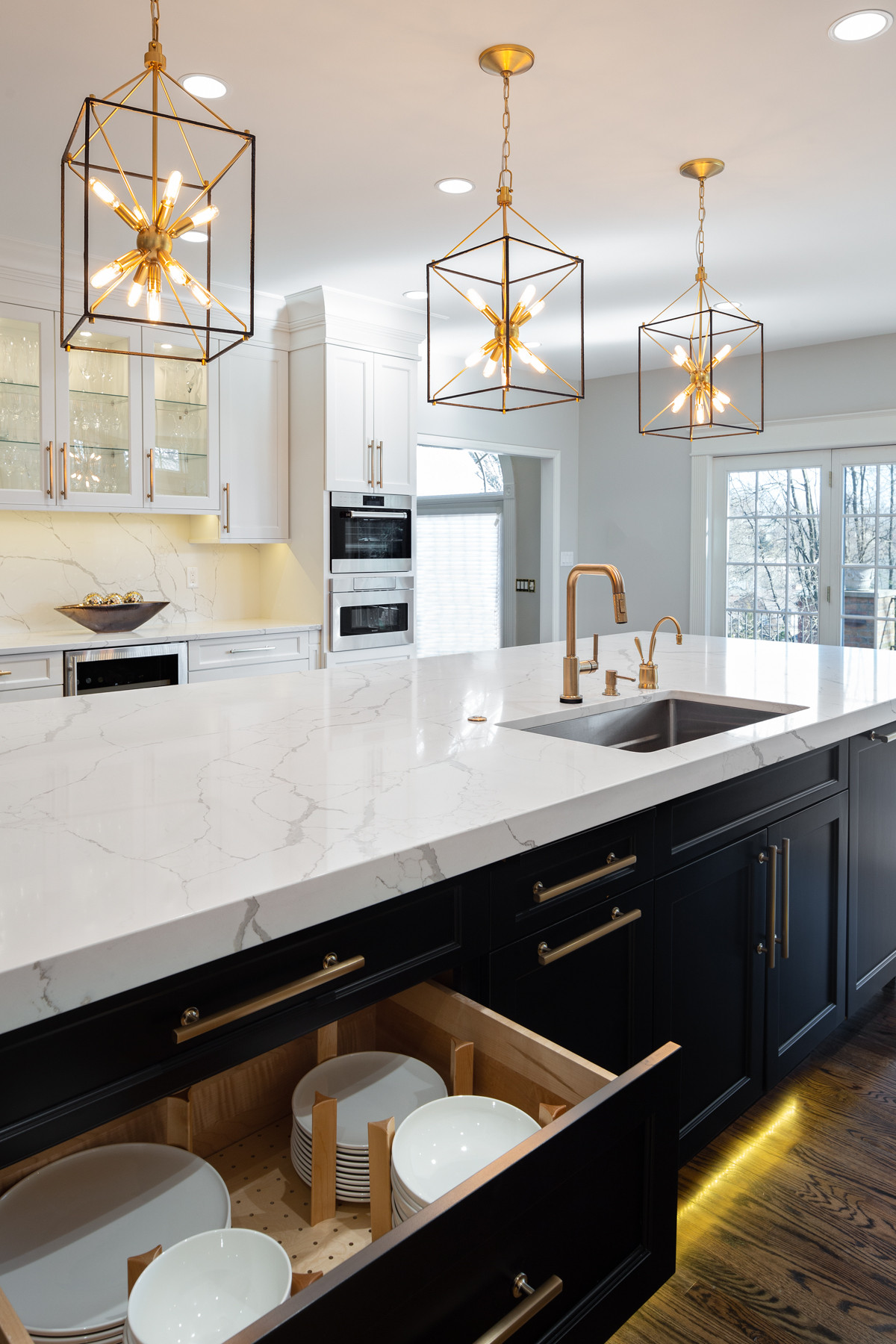 Contemporary kitchen with white marble countertops, black base cabinets, geometric gold pendant lights, and brass fixtures.
