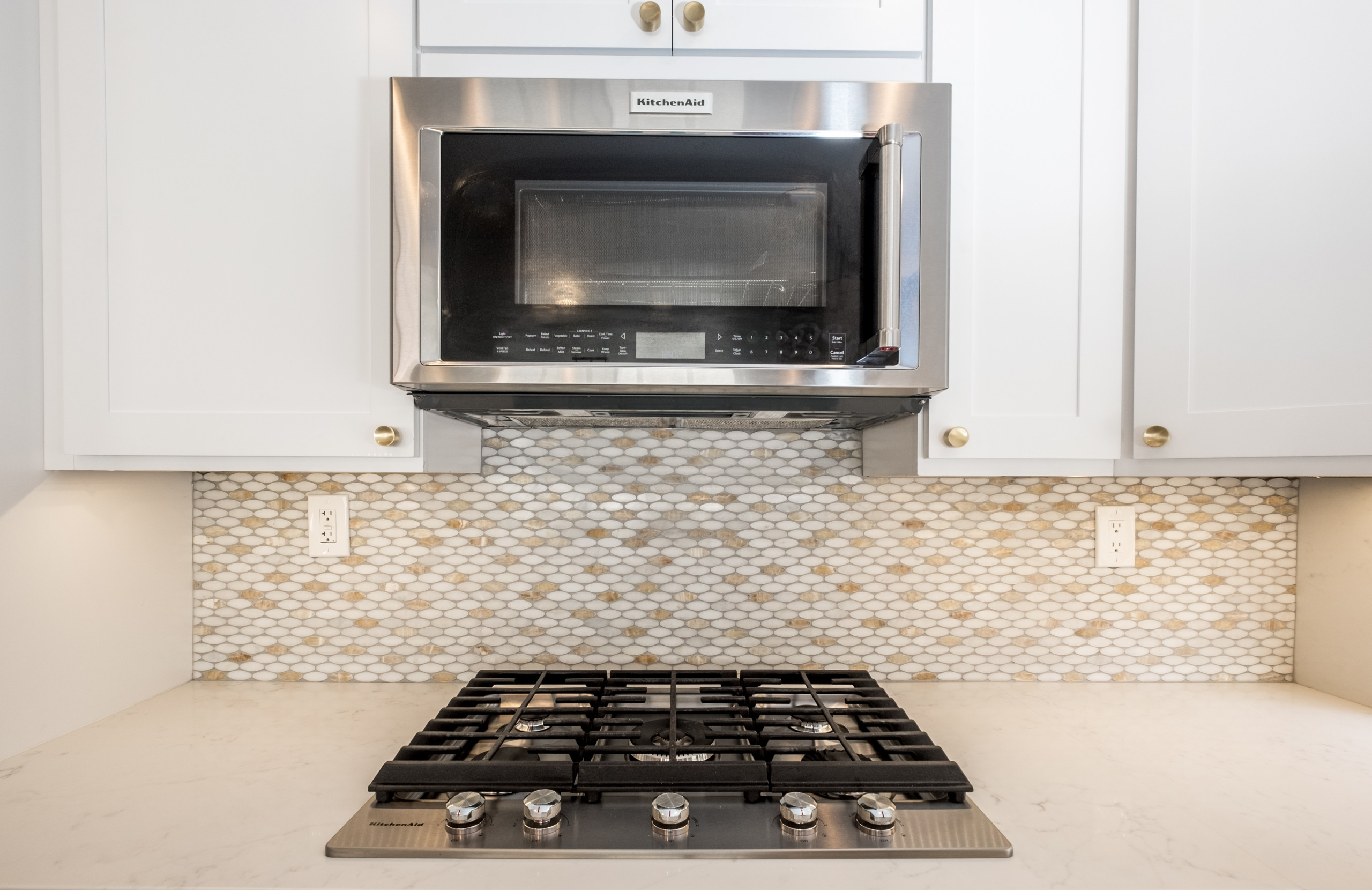 Modern kitchen featuring honeycomb pattern backsplash in white and gold, stainless steel appliances, and white cabinets with brass hardware.