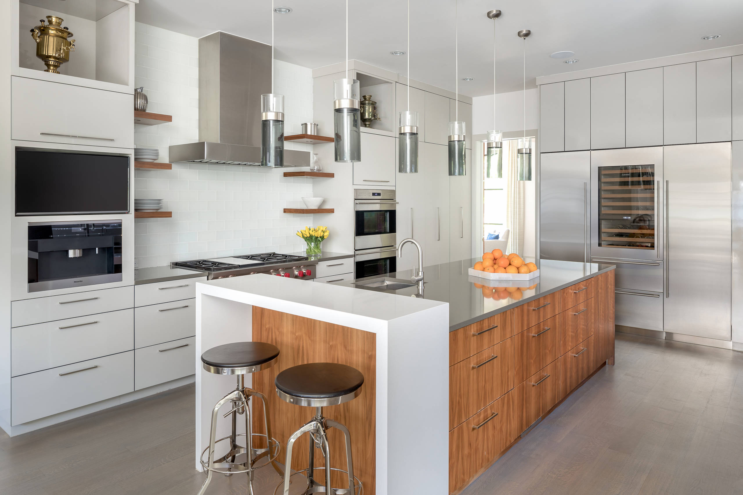 Modern kitchen featuring white cabinets, wooden accent island, floating shelves, glass pendant lights, and stainless steel appliances.