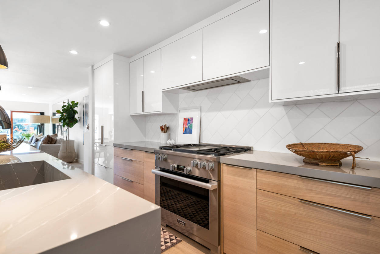 Modern kitchen featuring white upper cabinets, oak lower cabinets, diagonal tile backsplash, and stainless appliances with quartz countertops.