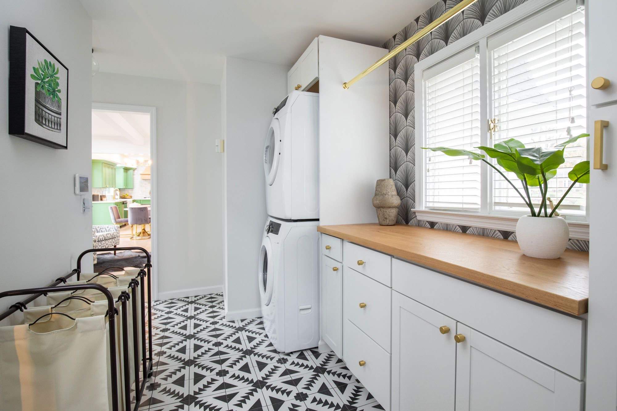 Laundry room with black and white geometric floor tiles, stacked washer-dryer, white cabinets, and art deco fan wallpaper.