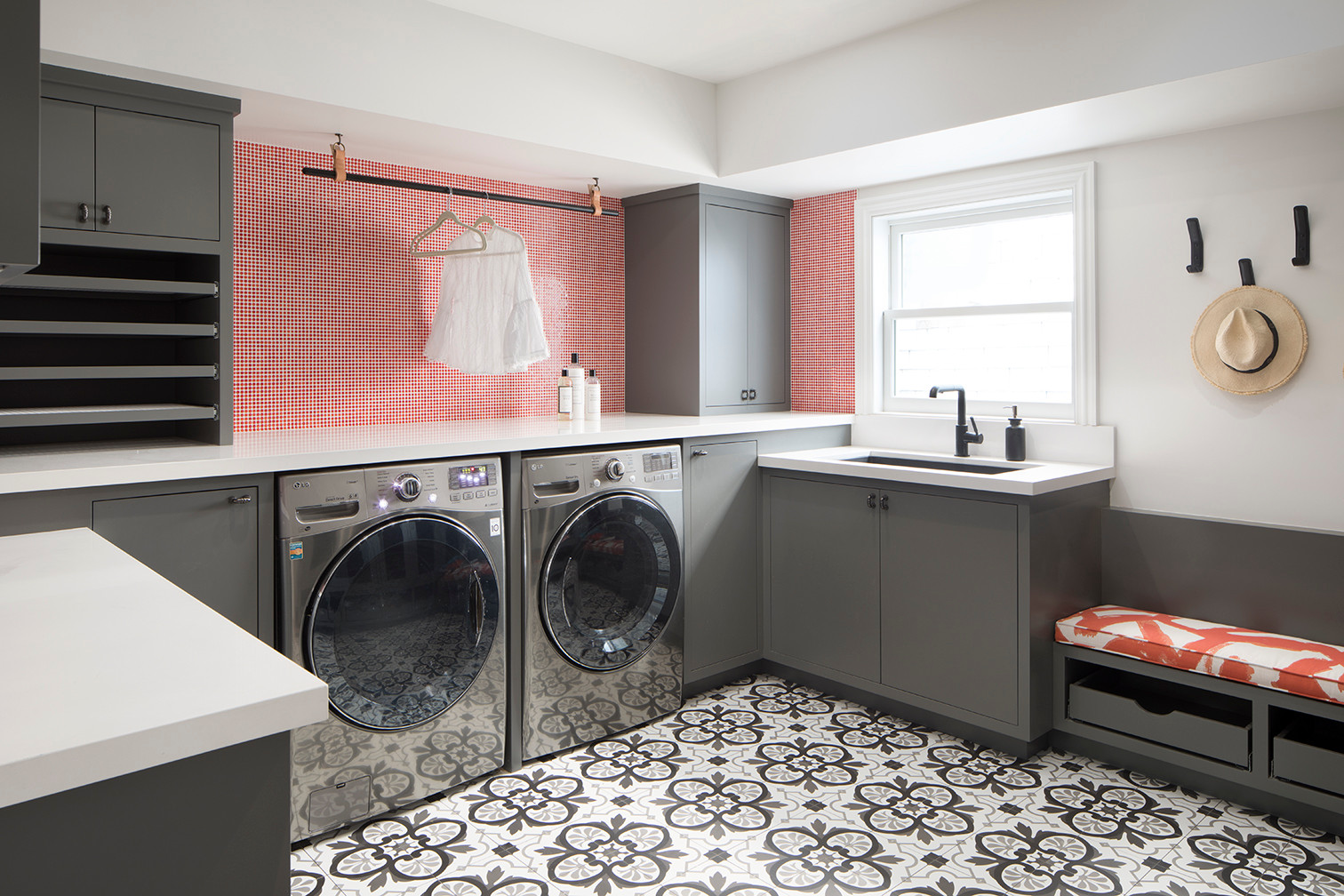 Laundry room with gray cabinets, coral geometric wallpaper, patterned floor tiles, and stainless steel appliances.