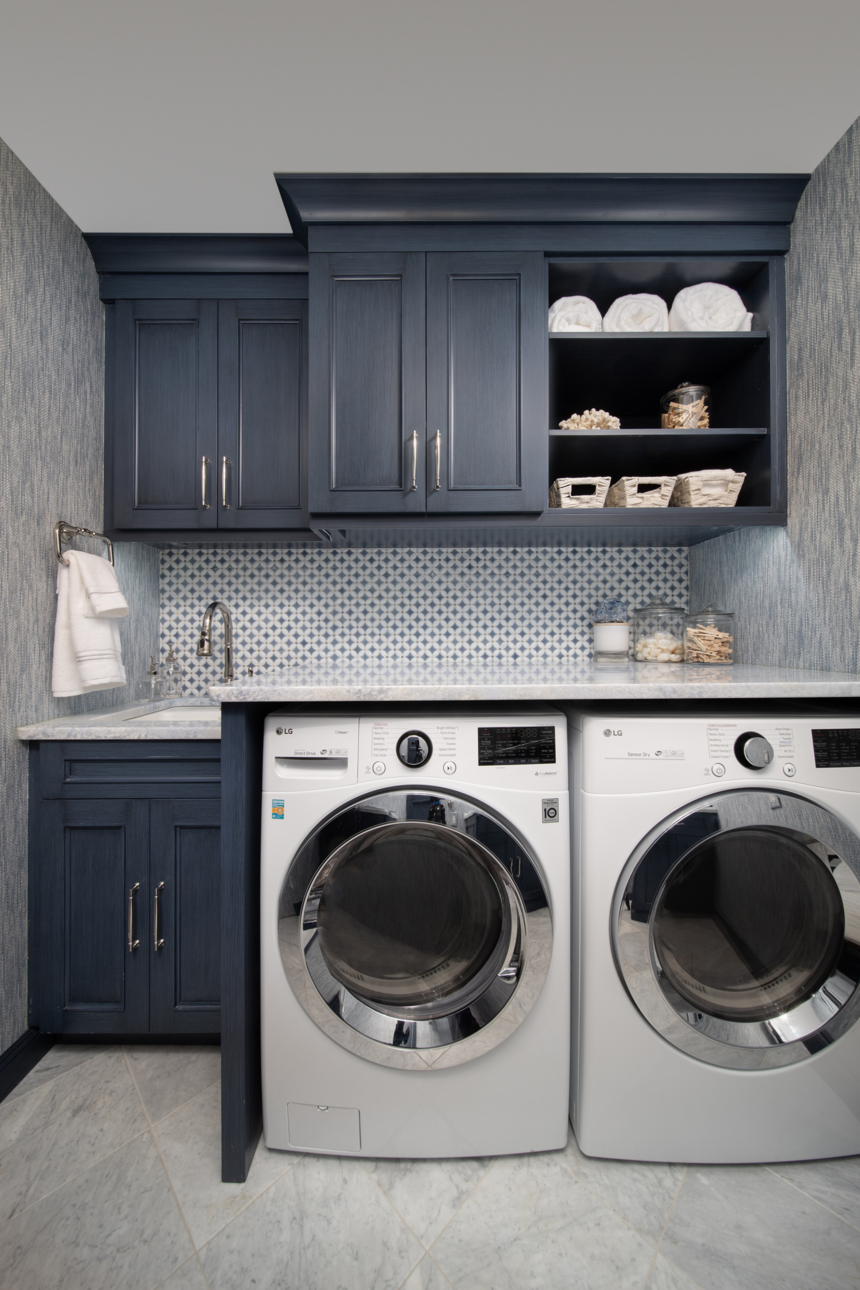 Laundry room featuring navy blue cabinets, patterned backsplash, marble countertops, and white front-loading appliances.