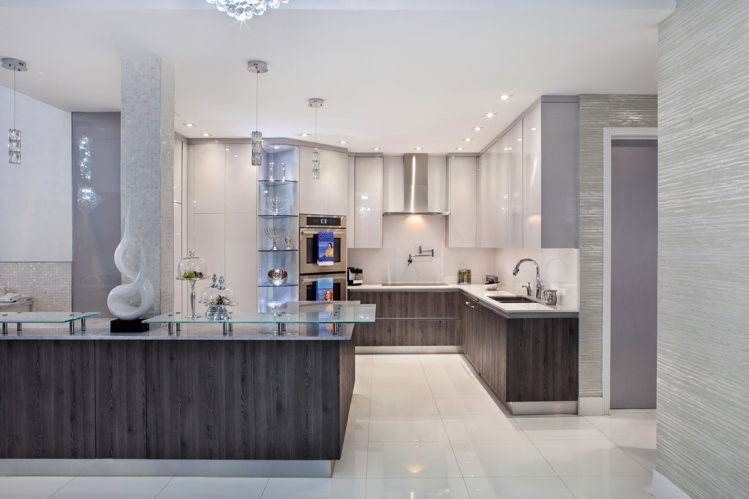 Modern L-shaped kitchen featuring dark wood base cabinets, white upper cabinets, glass display shelving, and crystal pendant lights.