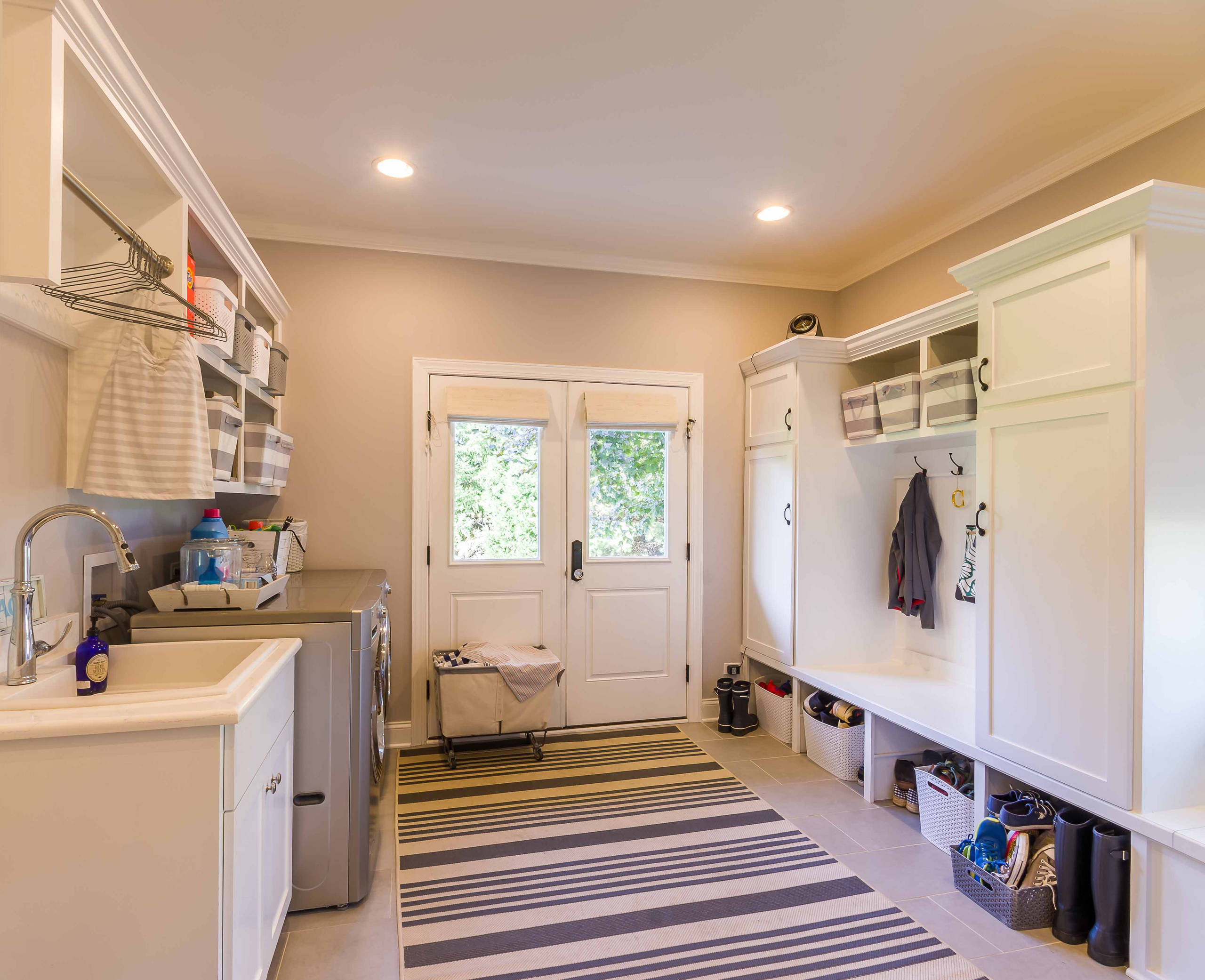 Bright mudroom combining laundry area with built-in white storage units, striped runner rug, and glass-paned double doors.