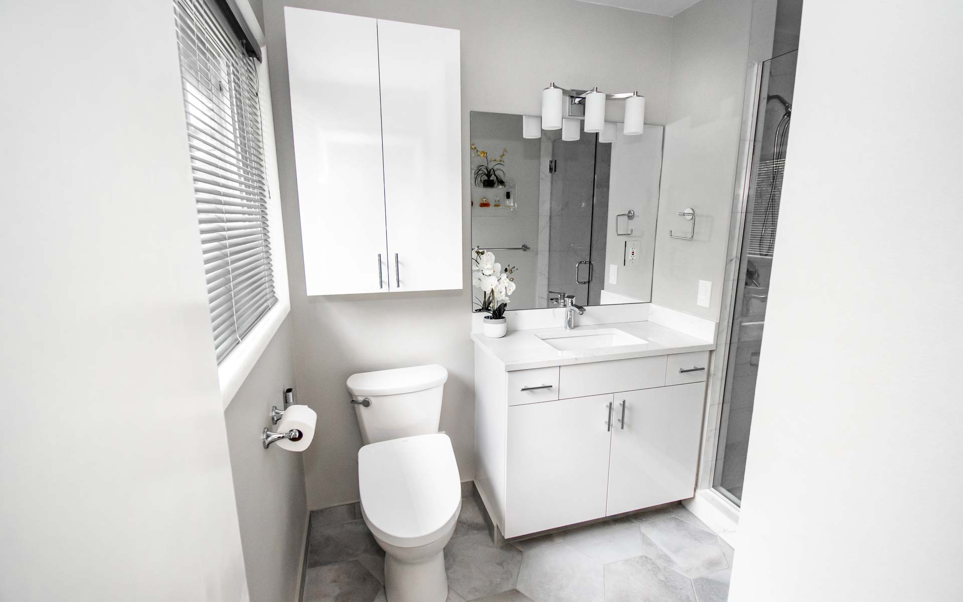 Modern white bathroom featuring marble floors, glass shower enclosure, white vanity, and cylindrical pendant lights.