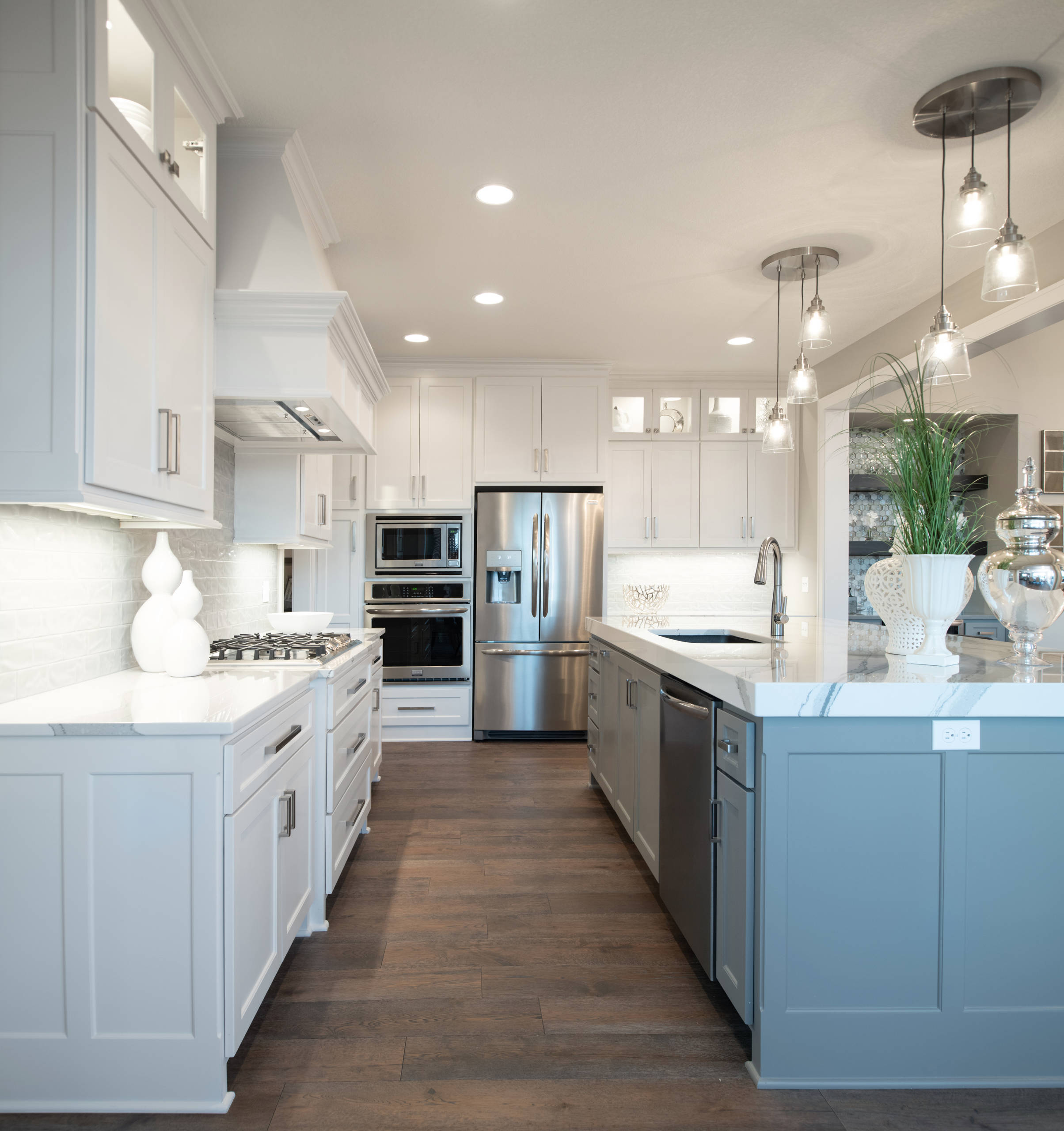 Bright white kitchen featuring blue accent island, glass pendant lights, stainless appliances, and wide plank hardwood floors.