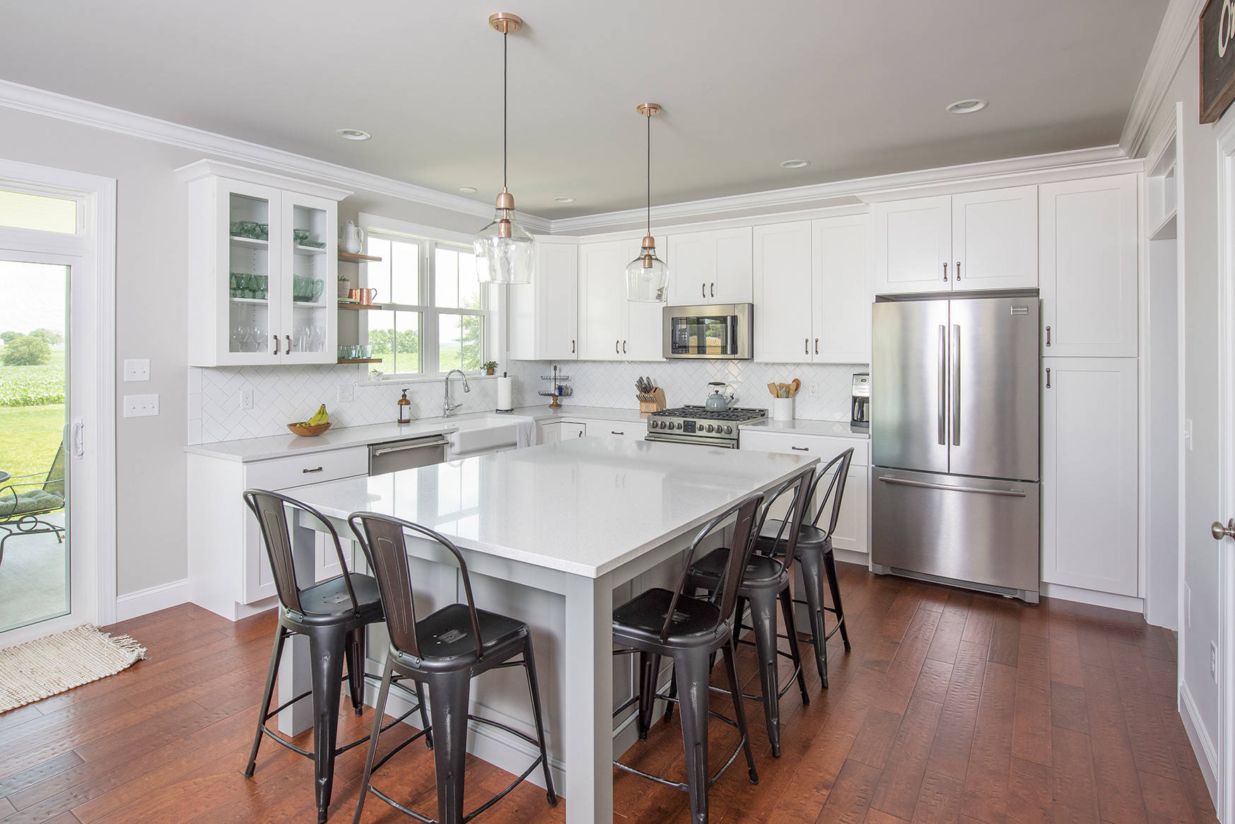 Bright white kitchen with large island, industrial metal barstools, glass pendant lights, and herringbone backsplash against stainless appliances.