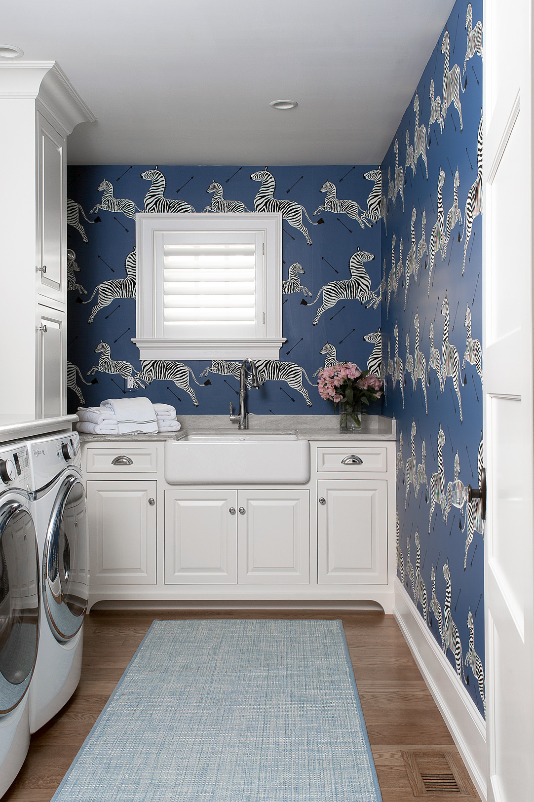Laundry room with navy zebra wallpaper, white cabinets, farmhouse sink, blue runner rug, and modern appliances.