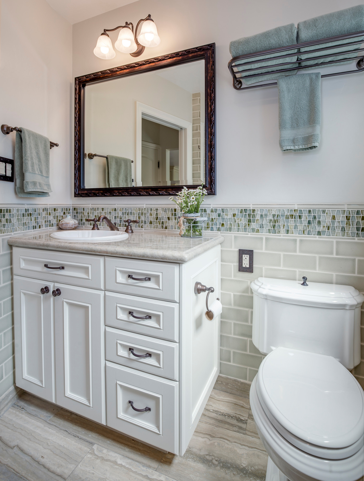 Transitional bathroom featuring white vanity, mosaic glass tile backsplash, bronze-framed mirror, and sage green accents.