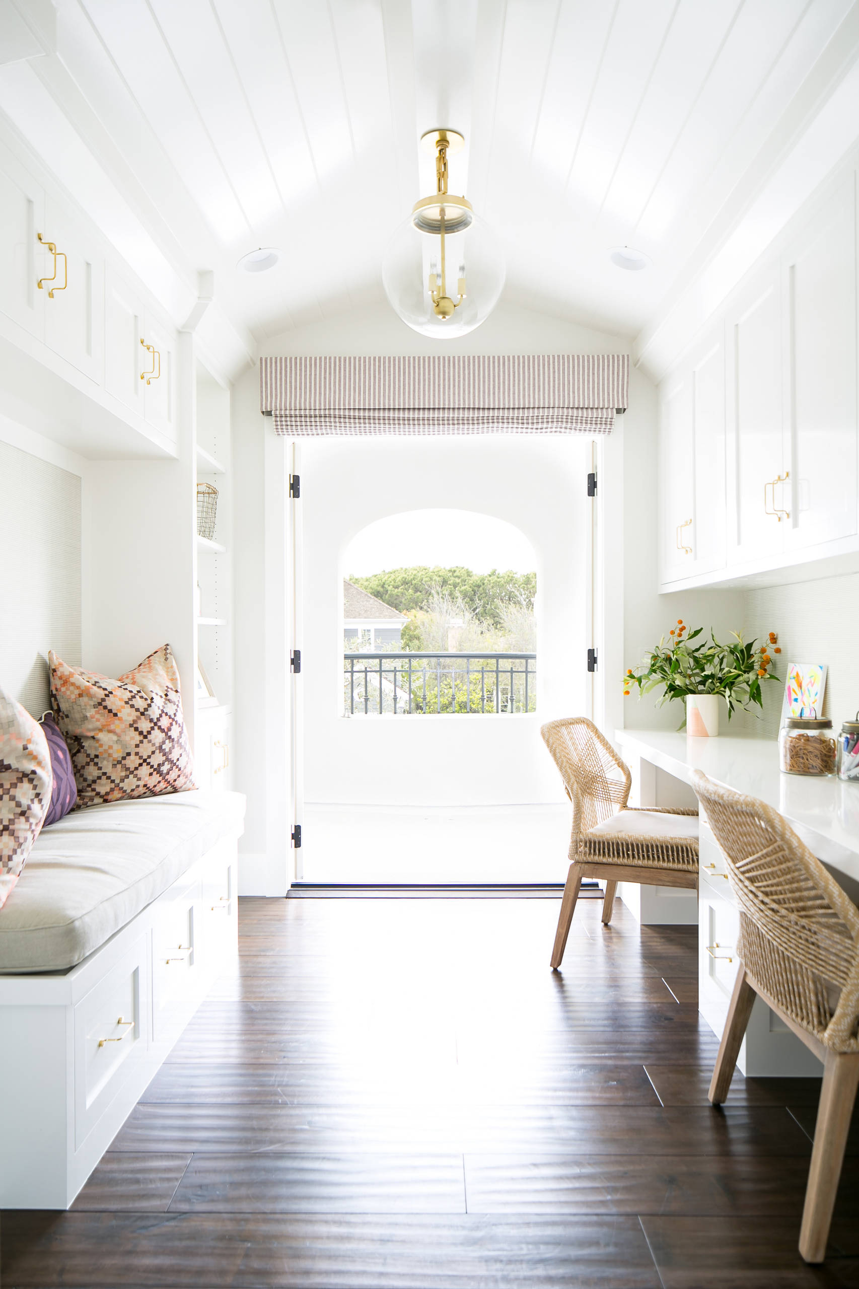 Bright, narrow room with built-in white cabinetry, a desk nook, and a bench with patterned pillows leading to a balcony.