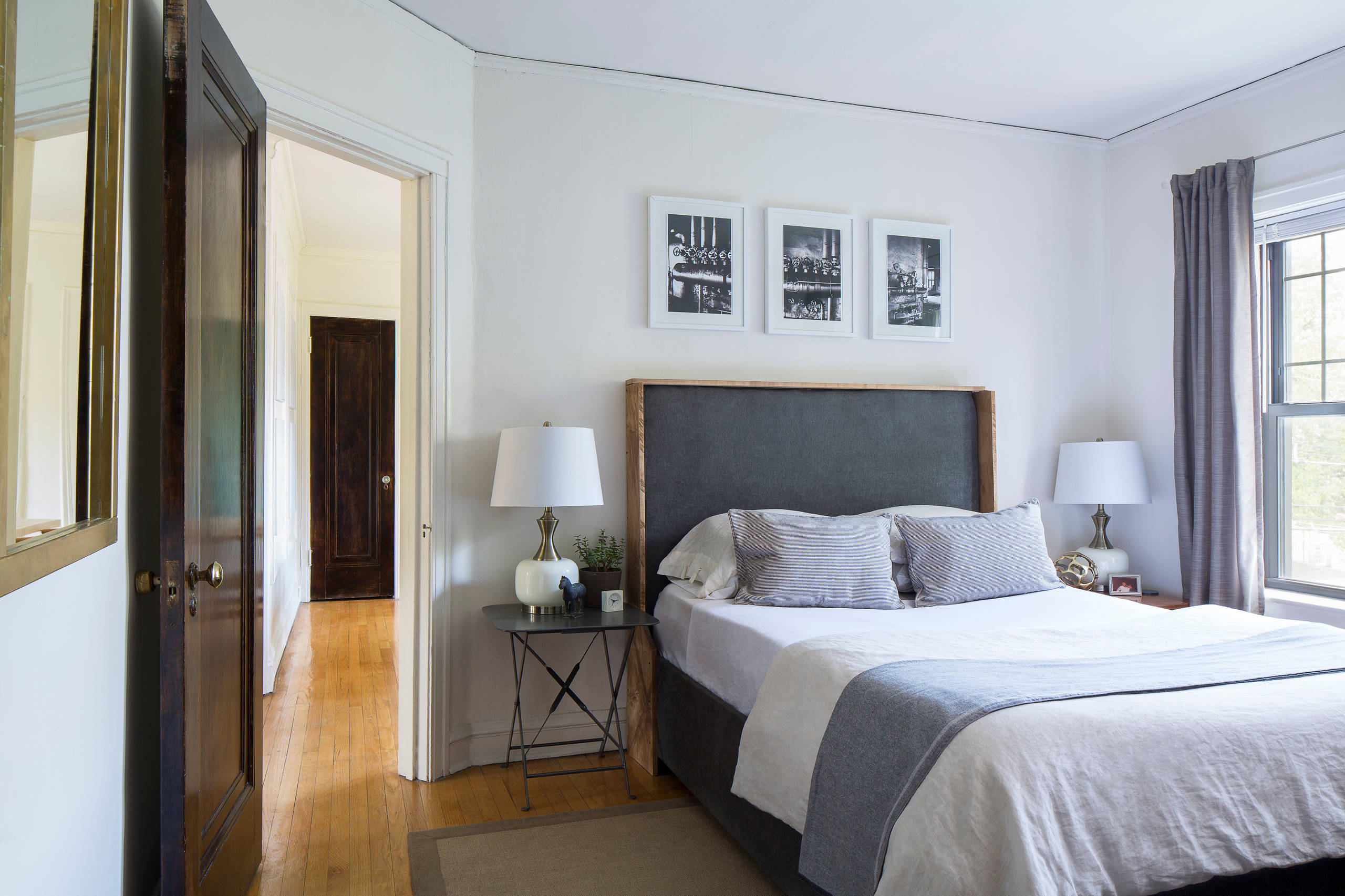 Bedroom with wood and charcoal upholstered bed, white bedding, black-and-white art, industrial side tables.