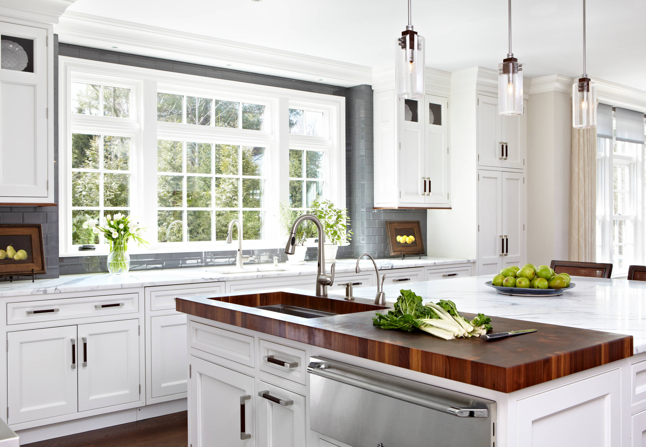 Bright kitchen with white shaker cabinets, gray subway tile, large windows, and a wood-topped island with a built-in sink.