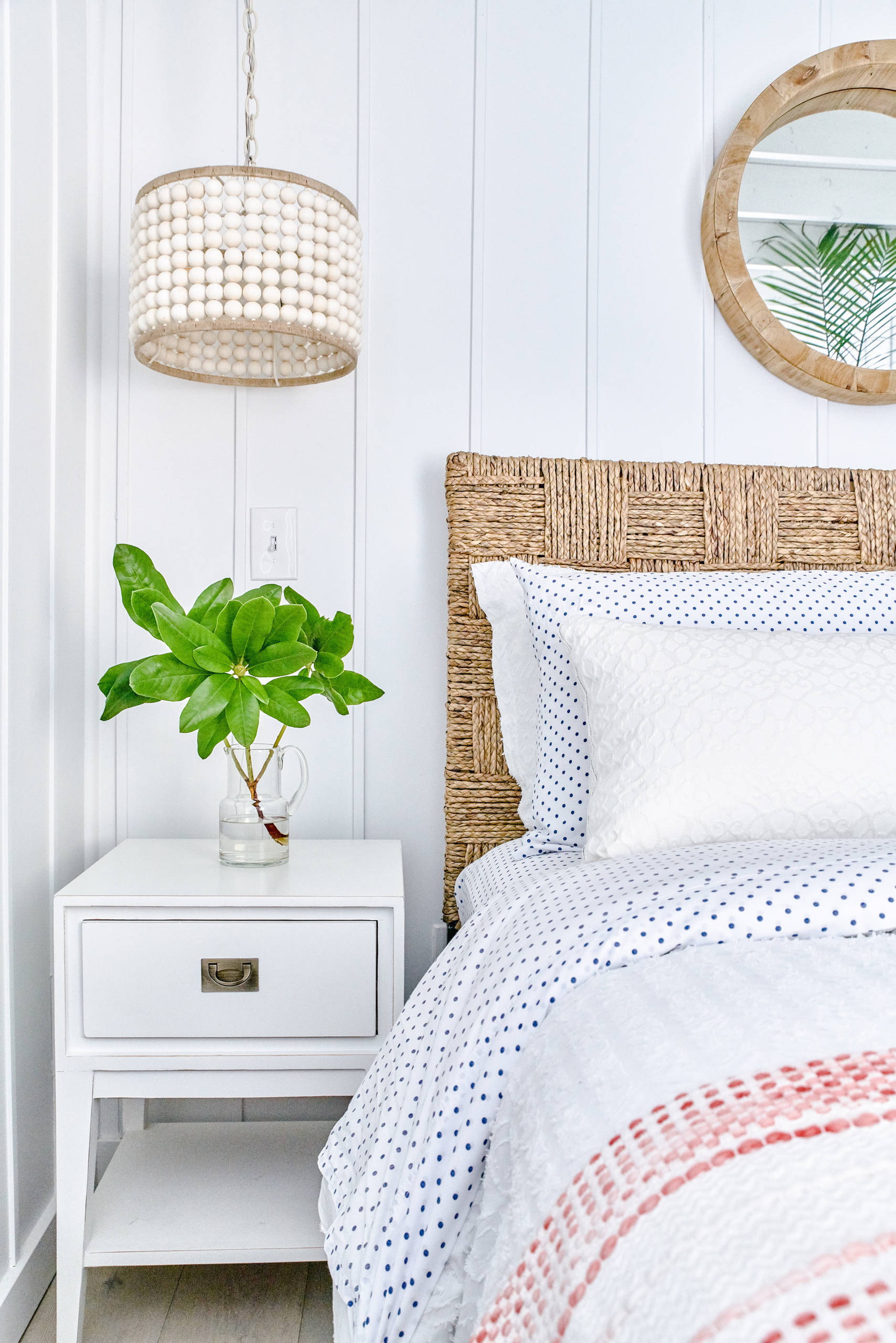 Bright bedroom with white shiplap walls, a woven headboard, and a beaded pendant light, featuring a green plant.