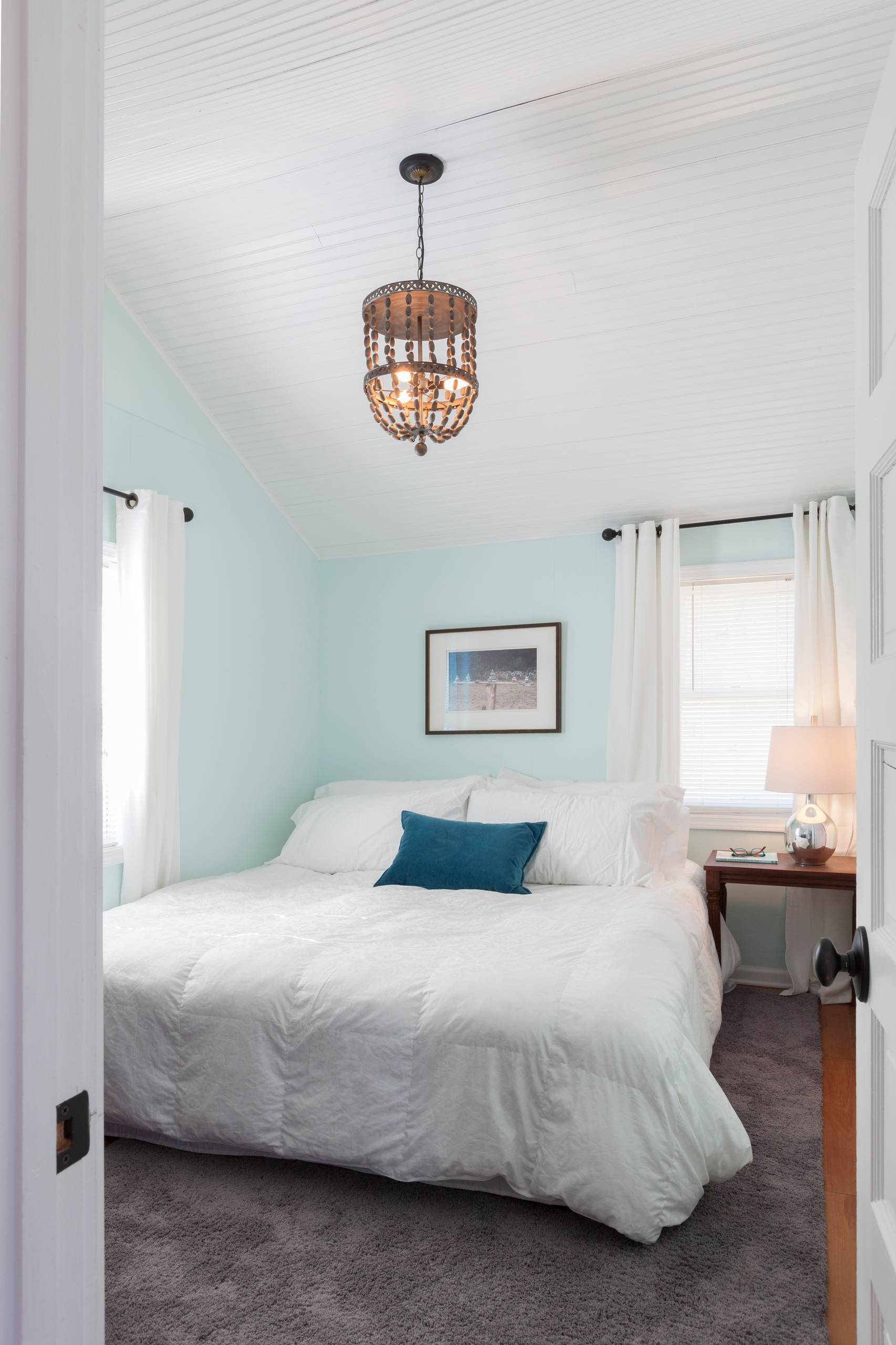 Bright bedroom with light blue walls, white beadboard ceiling, grey carpet, and a white bed.