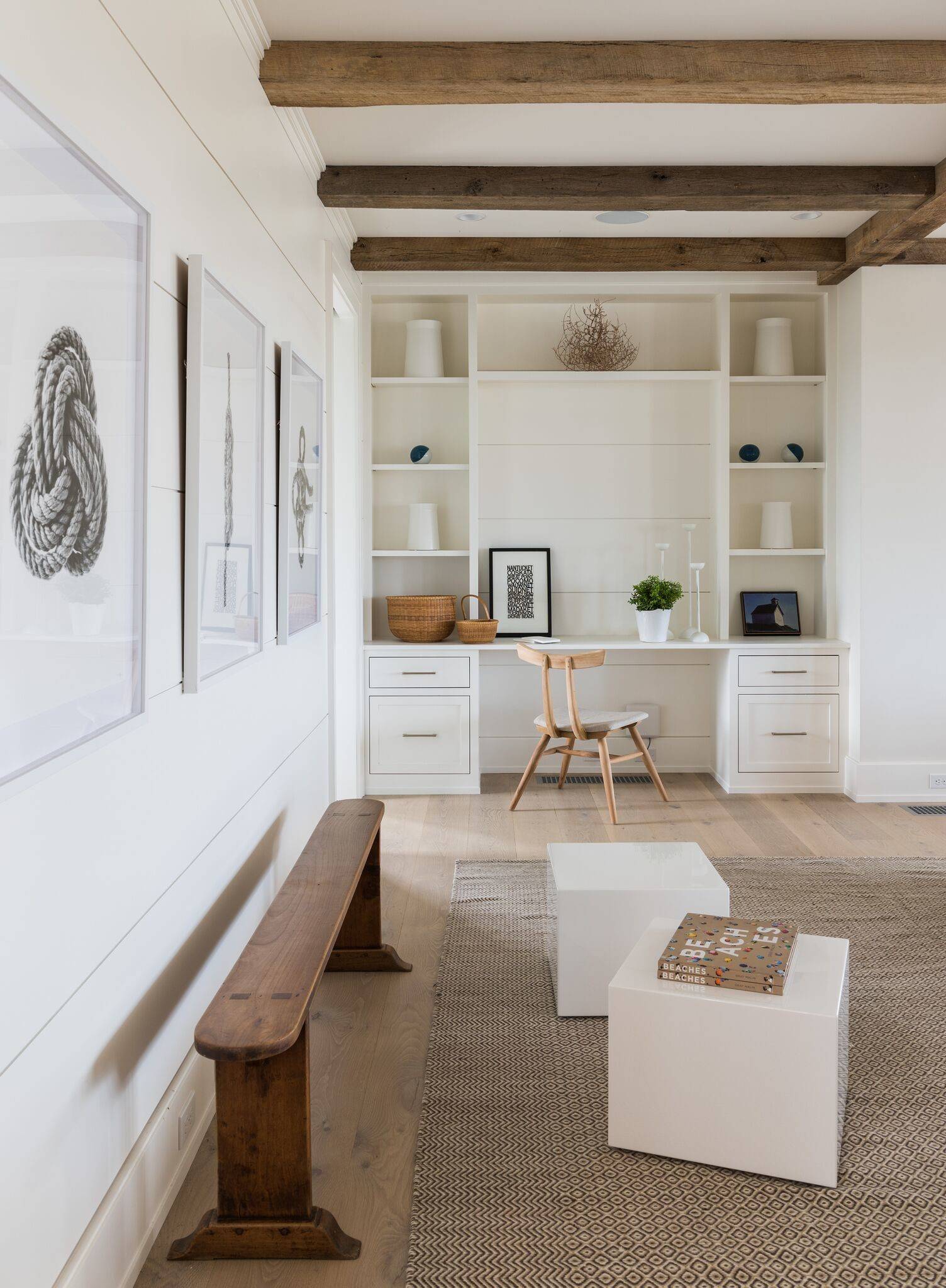 Bright home office with white built-in desk and shelving, light wood floors, and rustic ceiling beams.