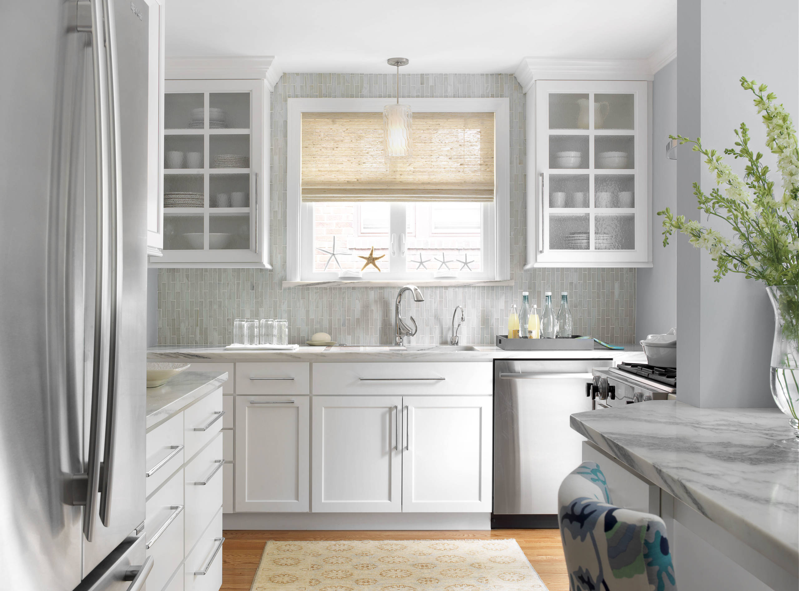 Bright kitchen with white cabinets, gray tile backsplash, marble countertops, stainless steel appliances, and a window with bamboo blinds.