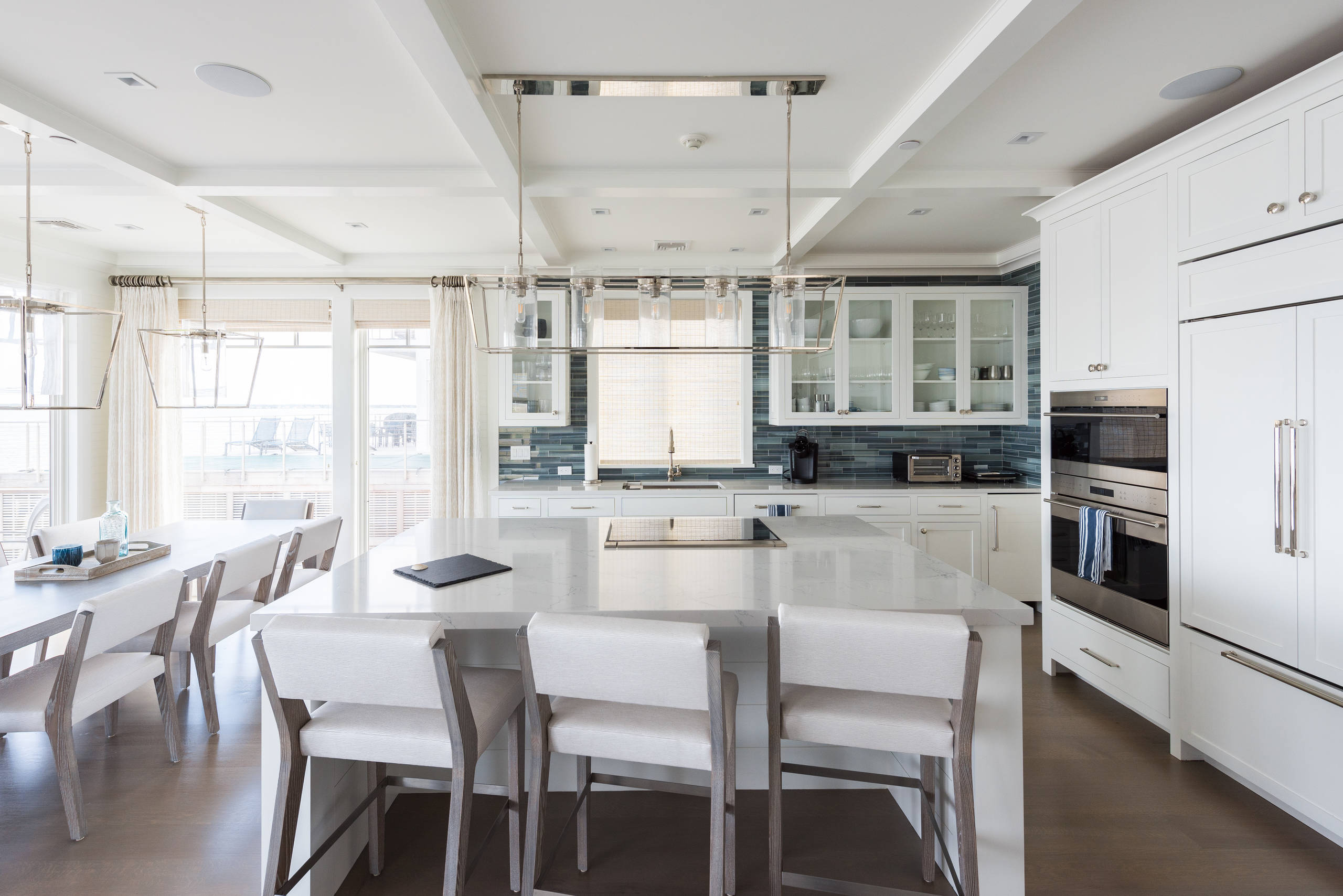 Bright, open-concept kitchen with white shaker cabinets, blue horizontal tile backsplash, large island with seating, and integrated dining area.