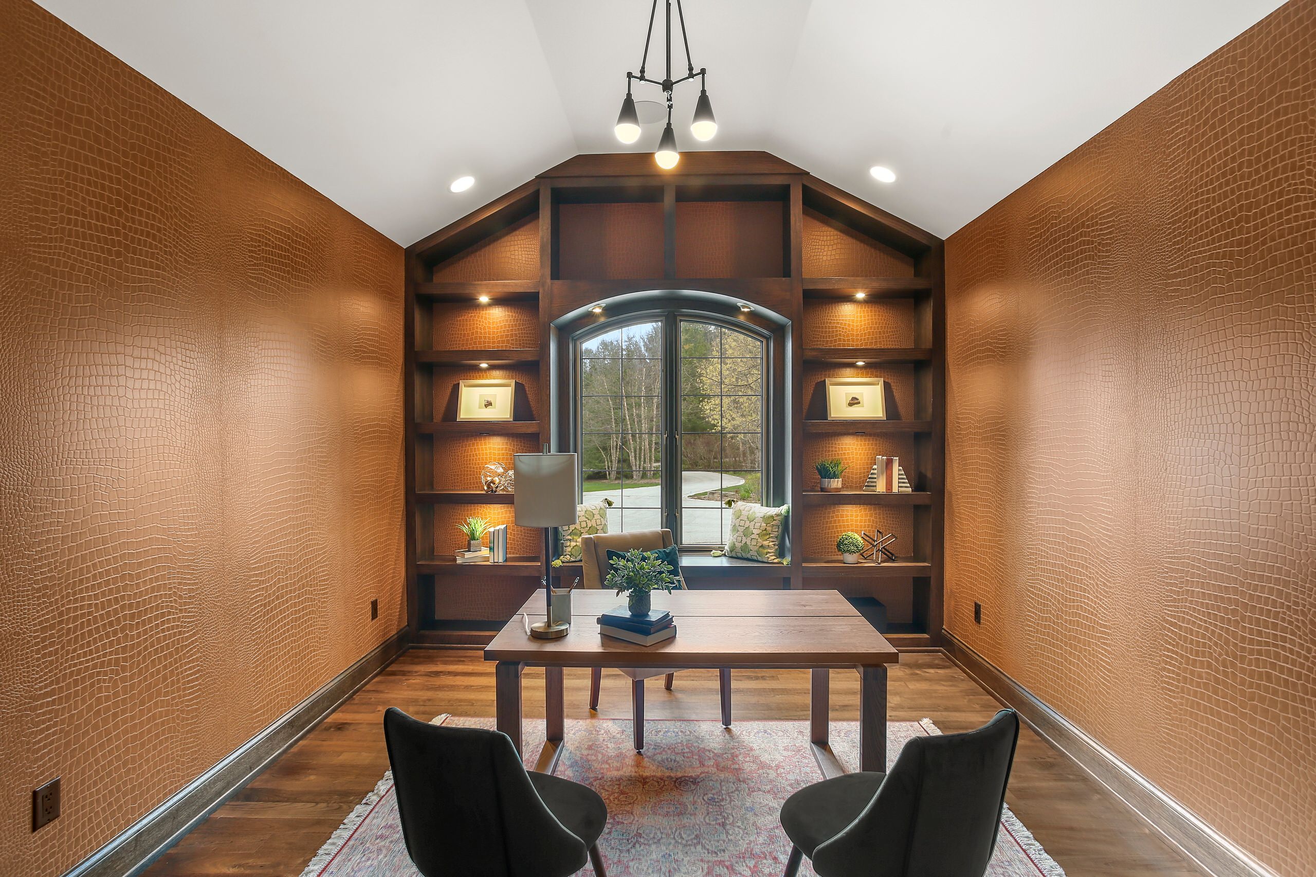 Home office with rich cognac alligator-textured walls, dark wood built-ins, arched window seat, and light wood desk.