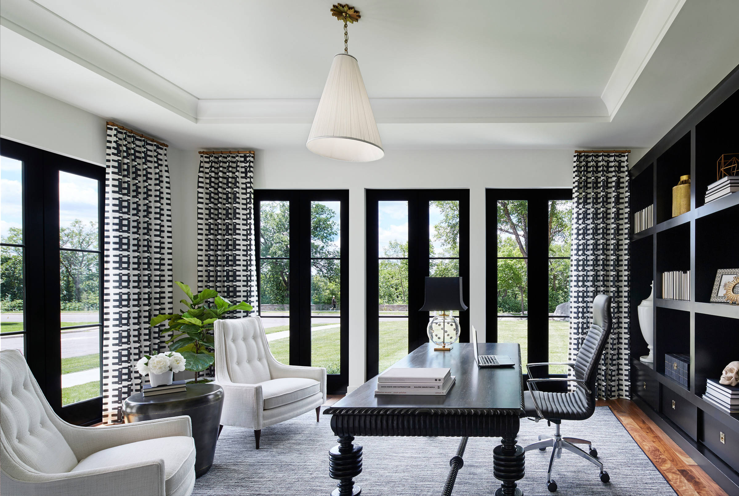 Contemporary home office with black built-in shelving, ornate dark wood desk, and patterned monochrome drapery.