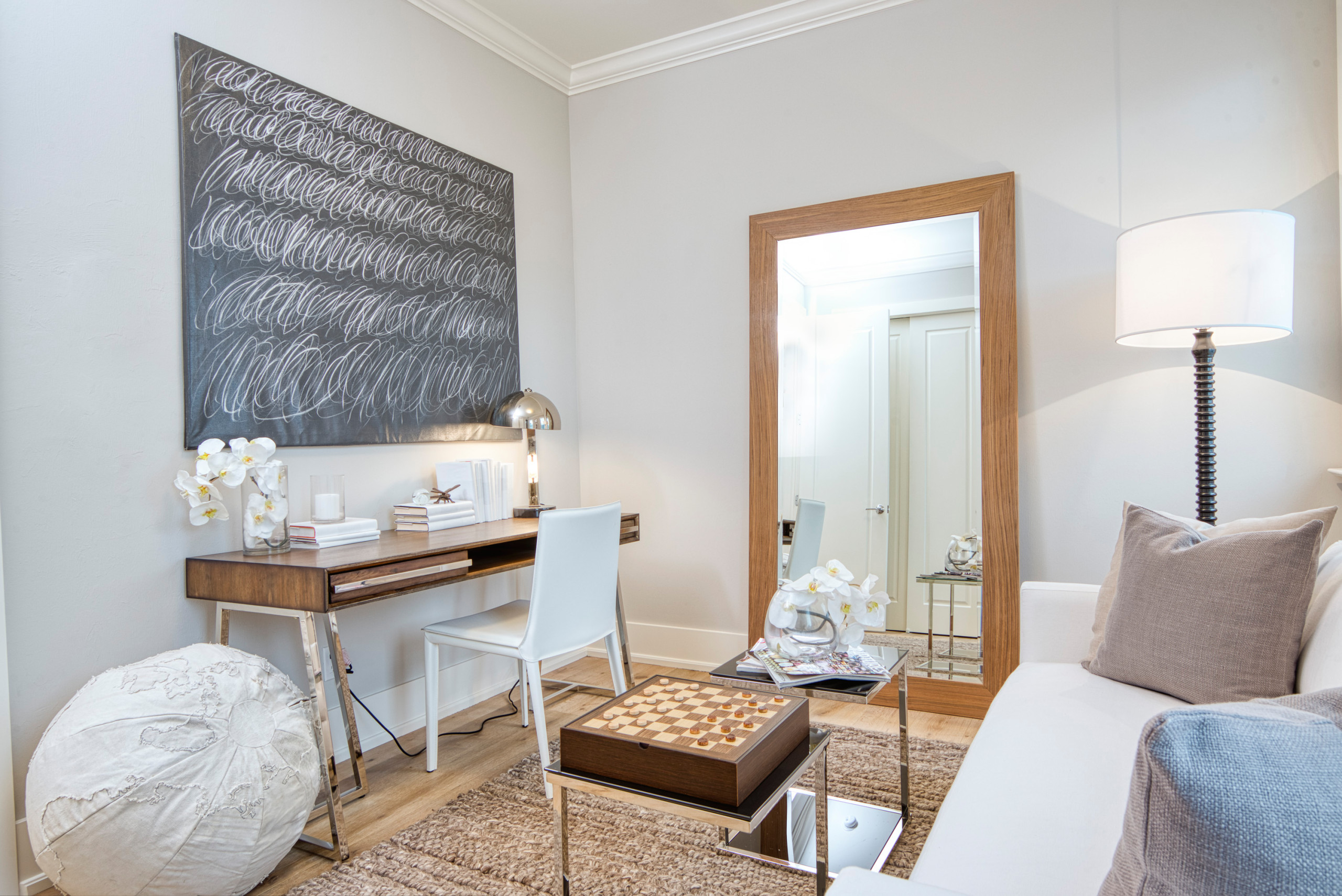 Neutral contemporary office den with wood desk, full-length mirror, white sofa, and textured rug.