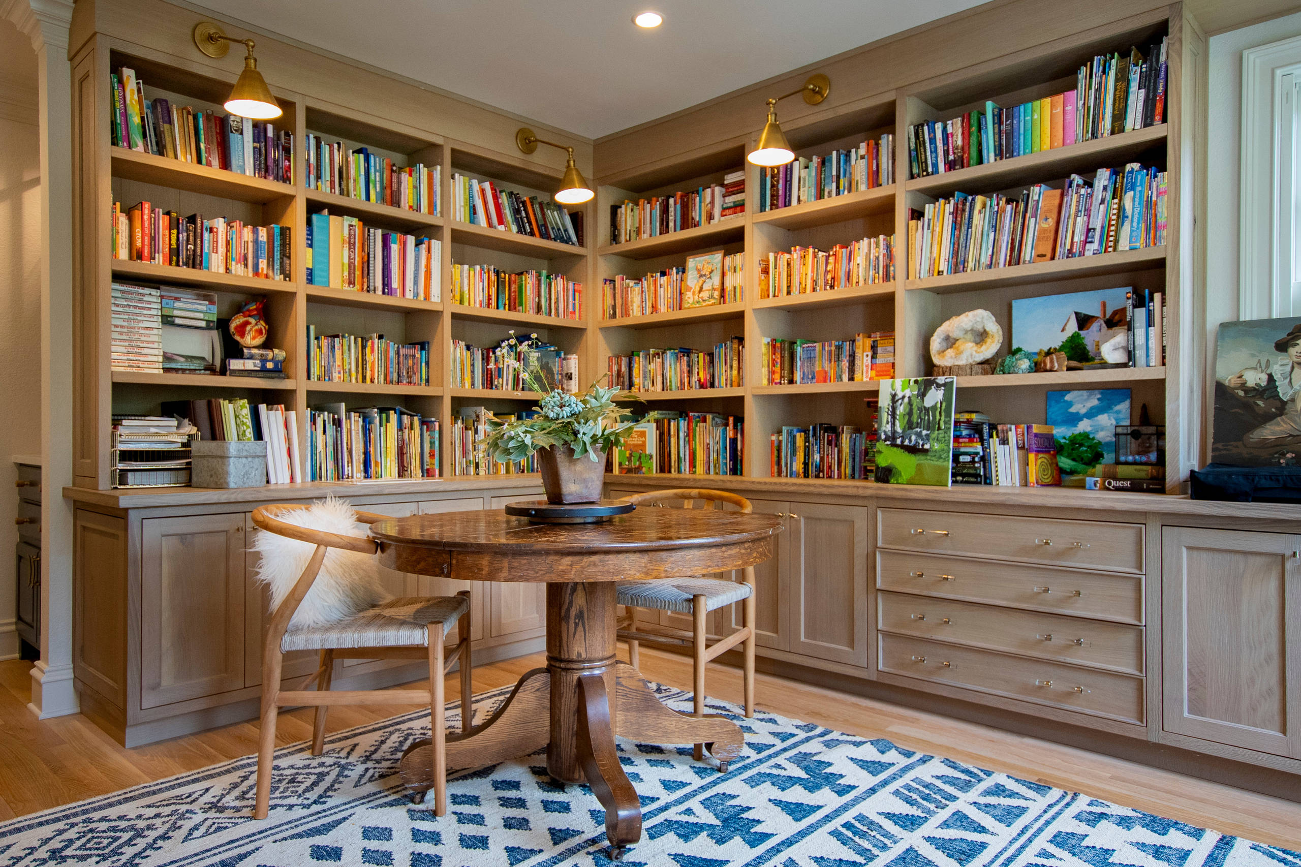 Cozy corner library with built-in wooden bookshelves, round table, two chairs, and blue patterned rug.