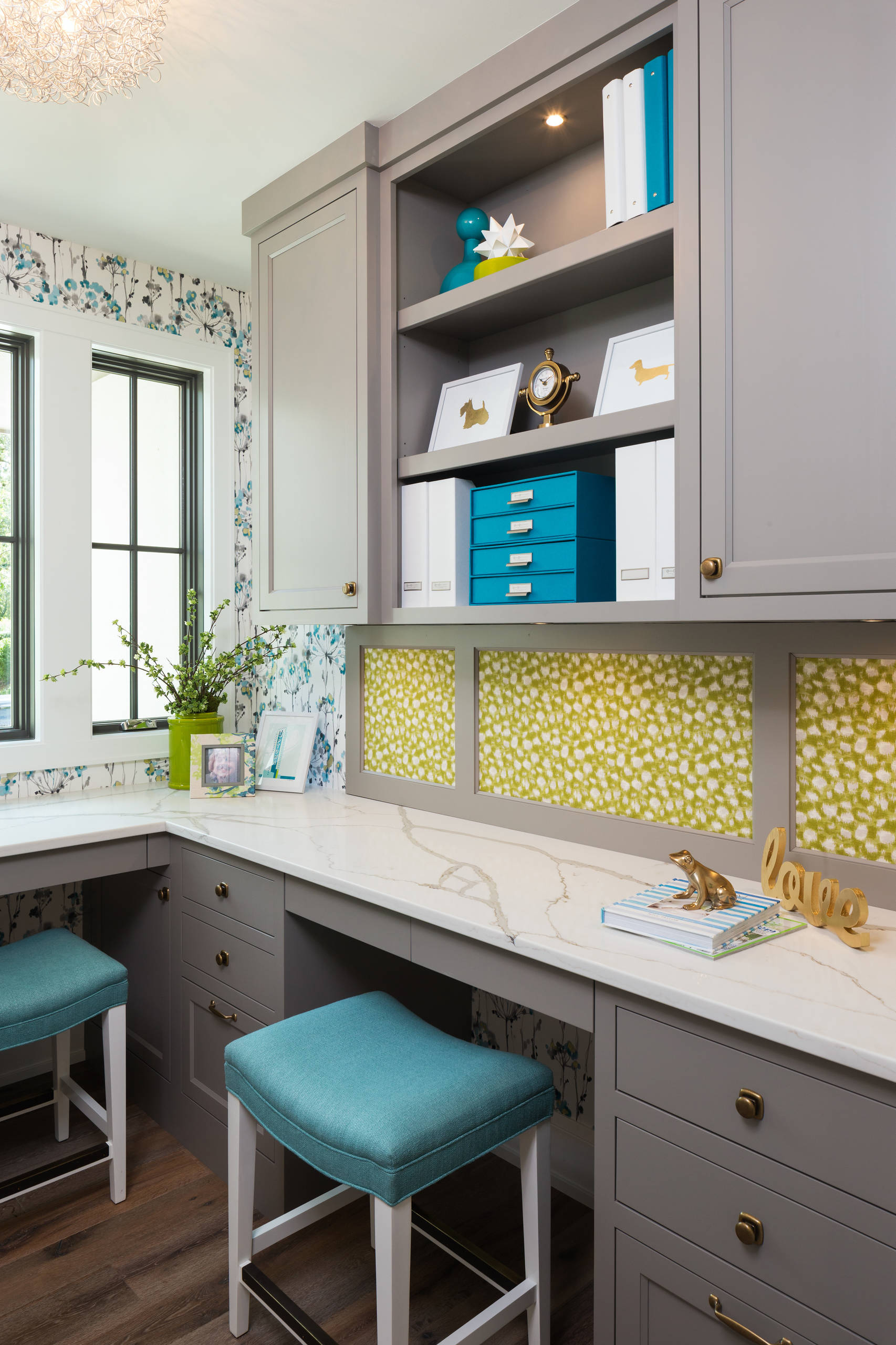 Bright corner office with grey cabinetry, white quartz countertops, teal stools, and botanical wallpaper.