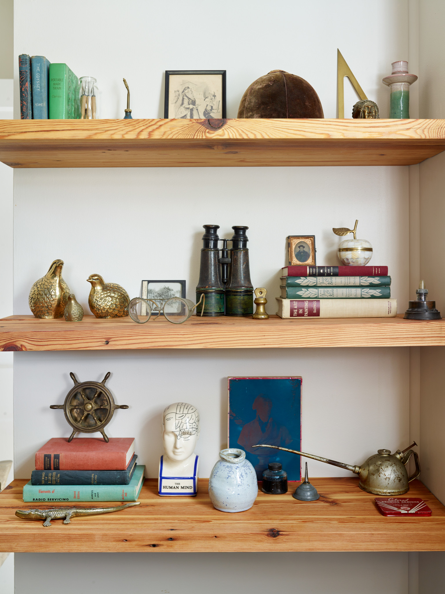 Three natural wood floating shelves display vintage books and an eclectic collection of brass objects and unique curios.