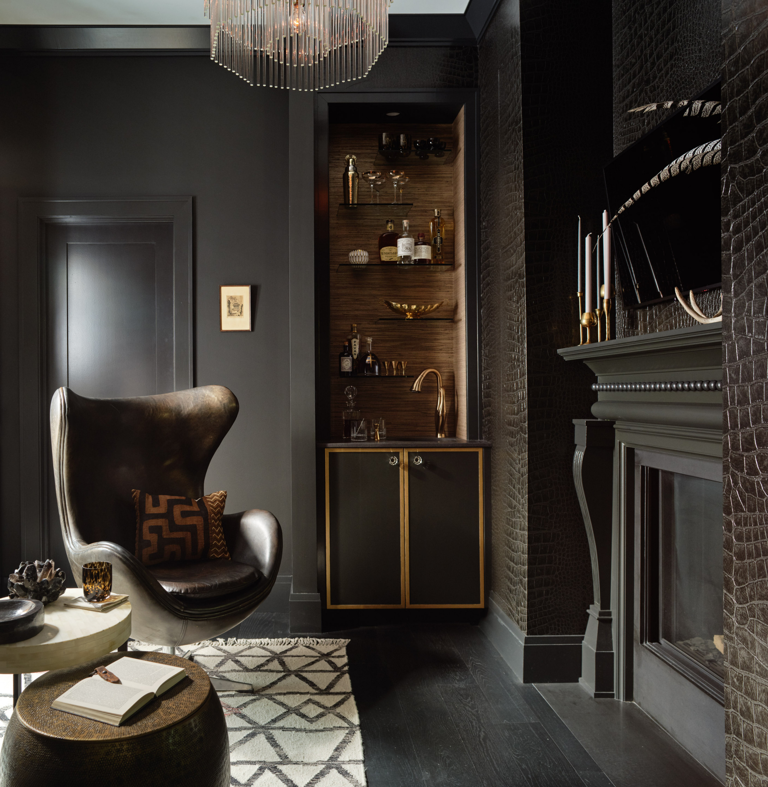 Moody dark gray living room with a rich leather armchair, built-in bar, and alligator textured wallpaper.