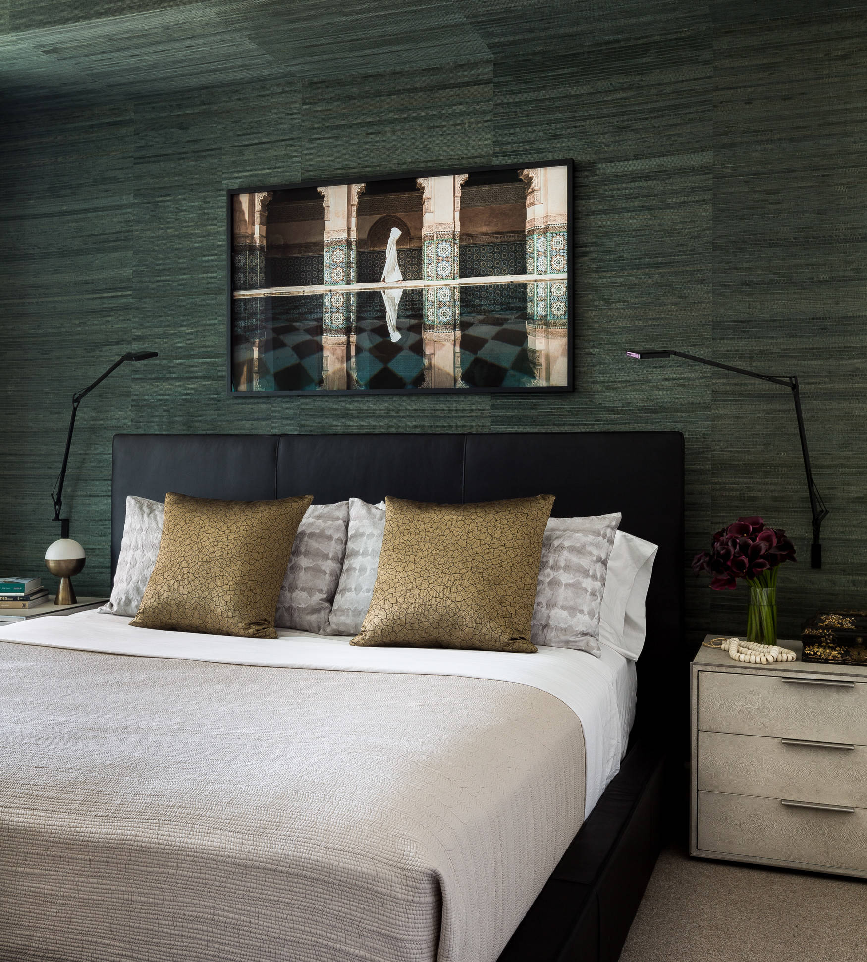 Bedroom with textured deep green walls, black leather bed, gold and grey cushions, and exotic artwork.