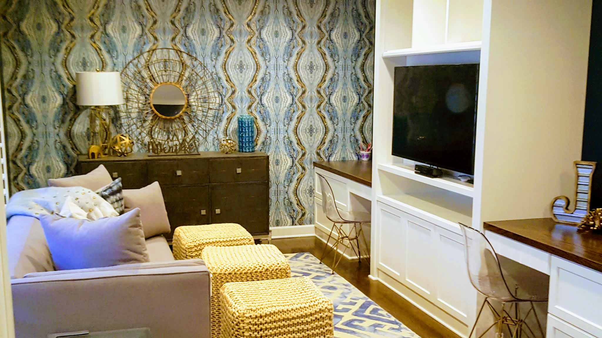 Eclectic living space featuring blue patterned wallpaper, a dark dresser, light sofa, and a built-in desk nook.