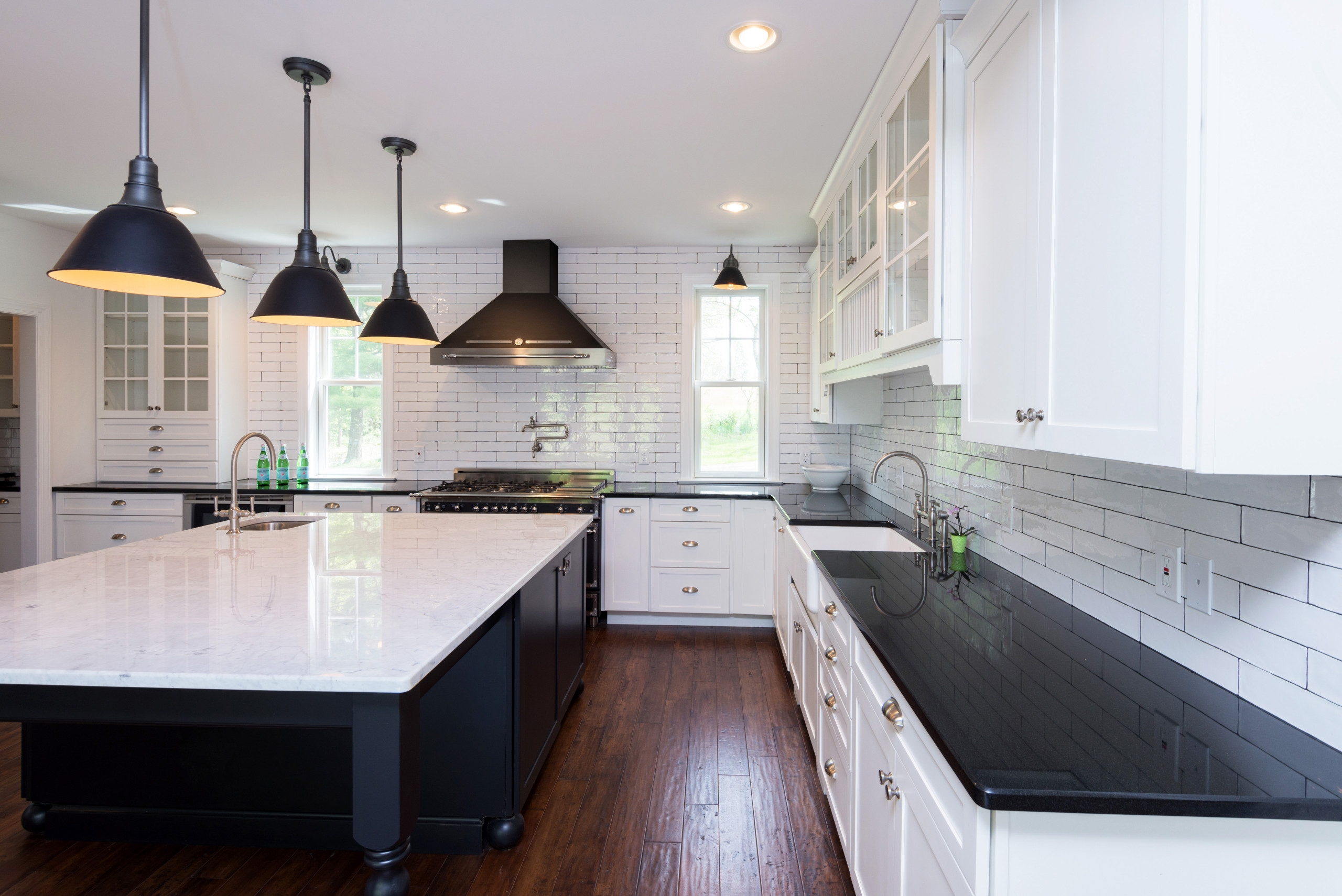 Spacious farmhouse kitchen with white subway tile backsplash, black range hood, and dark wood floors.